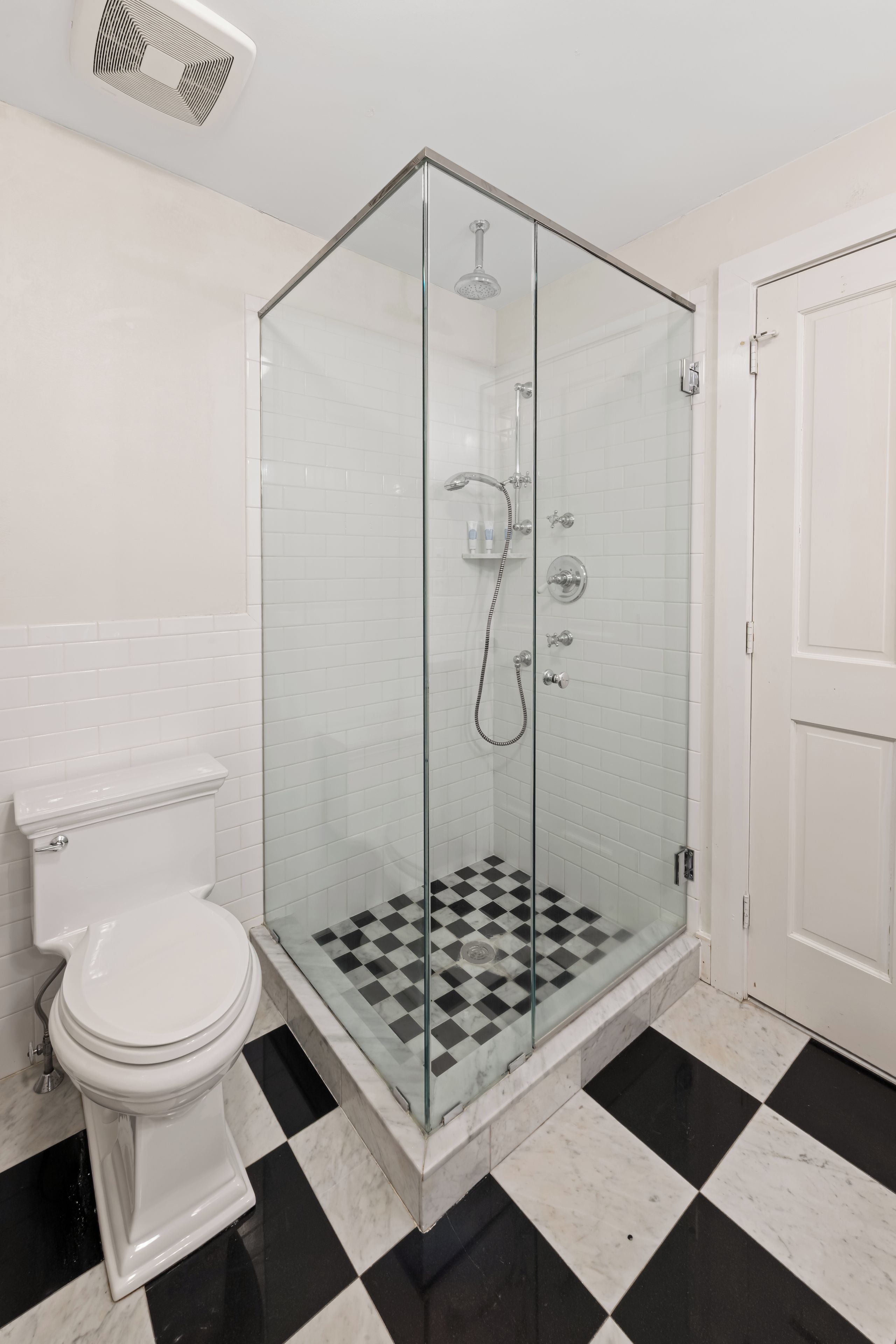 A bathroom with a glass-enclosed shower, a toilet, and a checkered floor.