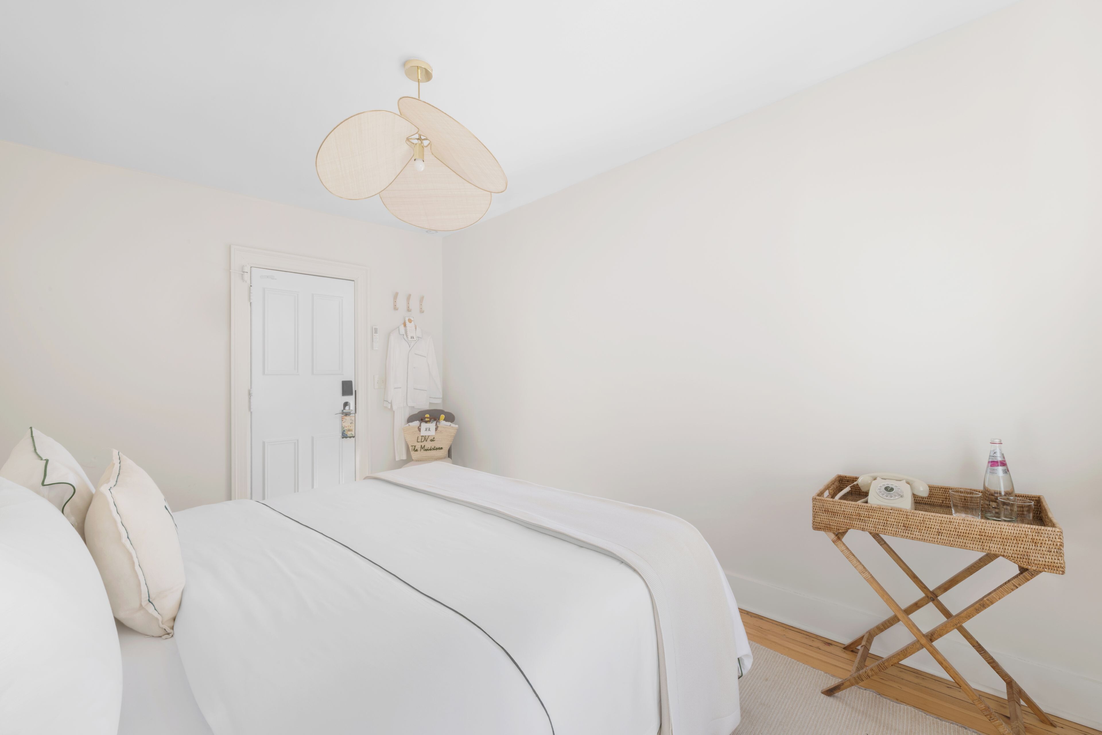 Un dormitorio con una cama, una mesita de noche con un teléfono y gafas, y una lámpara de pared.