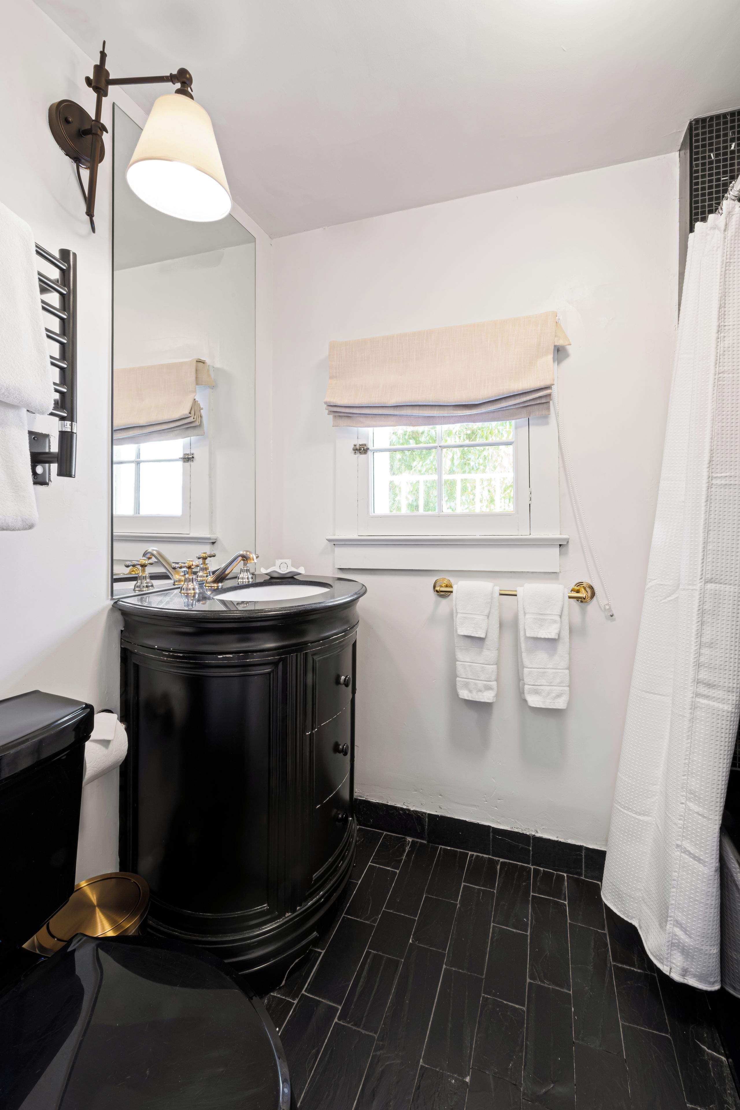 Een badkamer met een zwart wastafelmeubel, een spiegel, een raam met uitzicht en een handdoekrek.