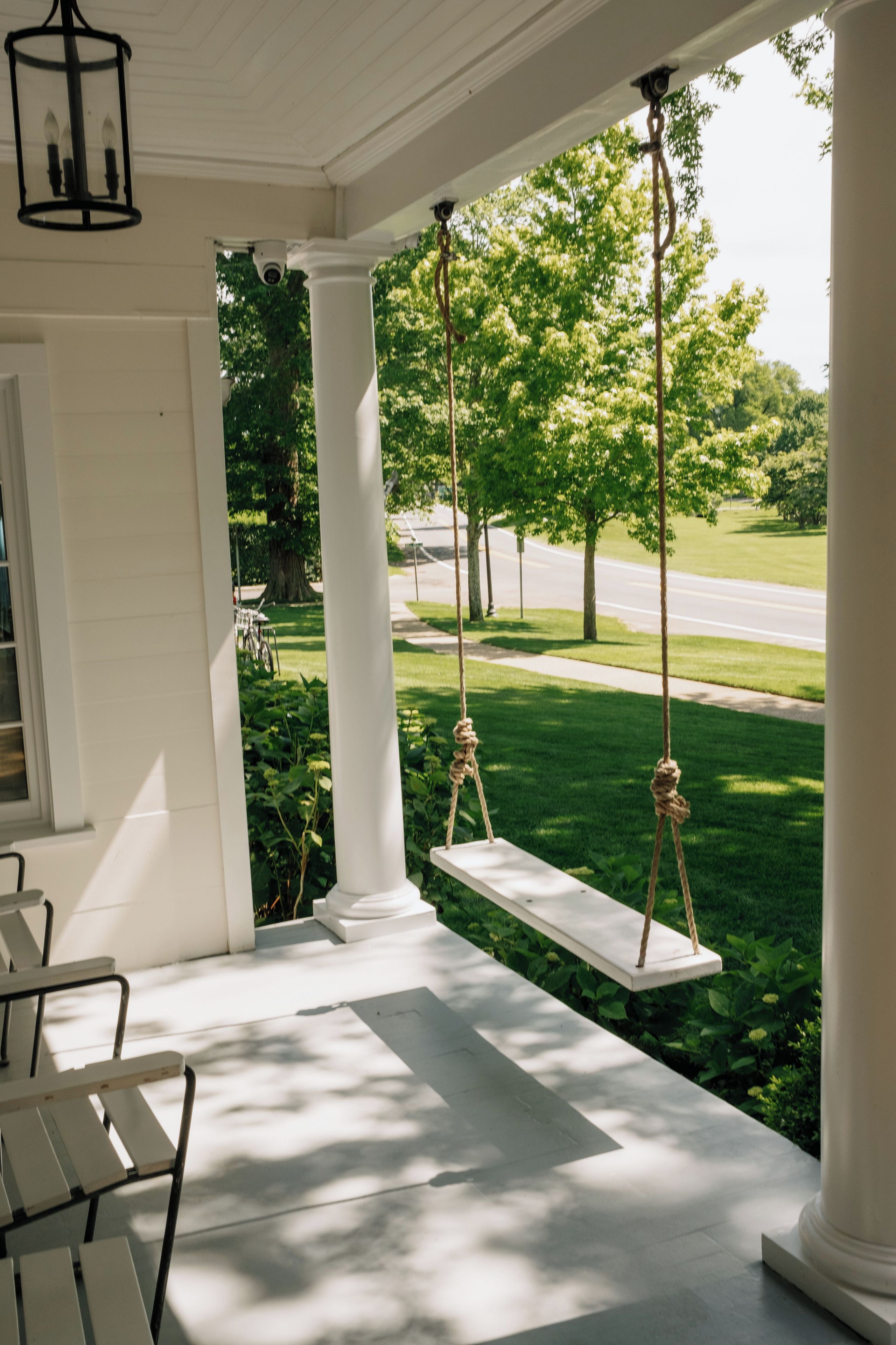 A porch with white columns, a swing, and a view of a green lawn and trees.