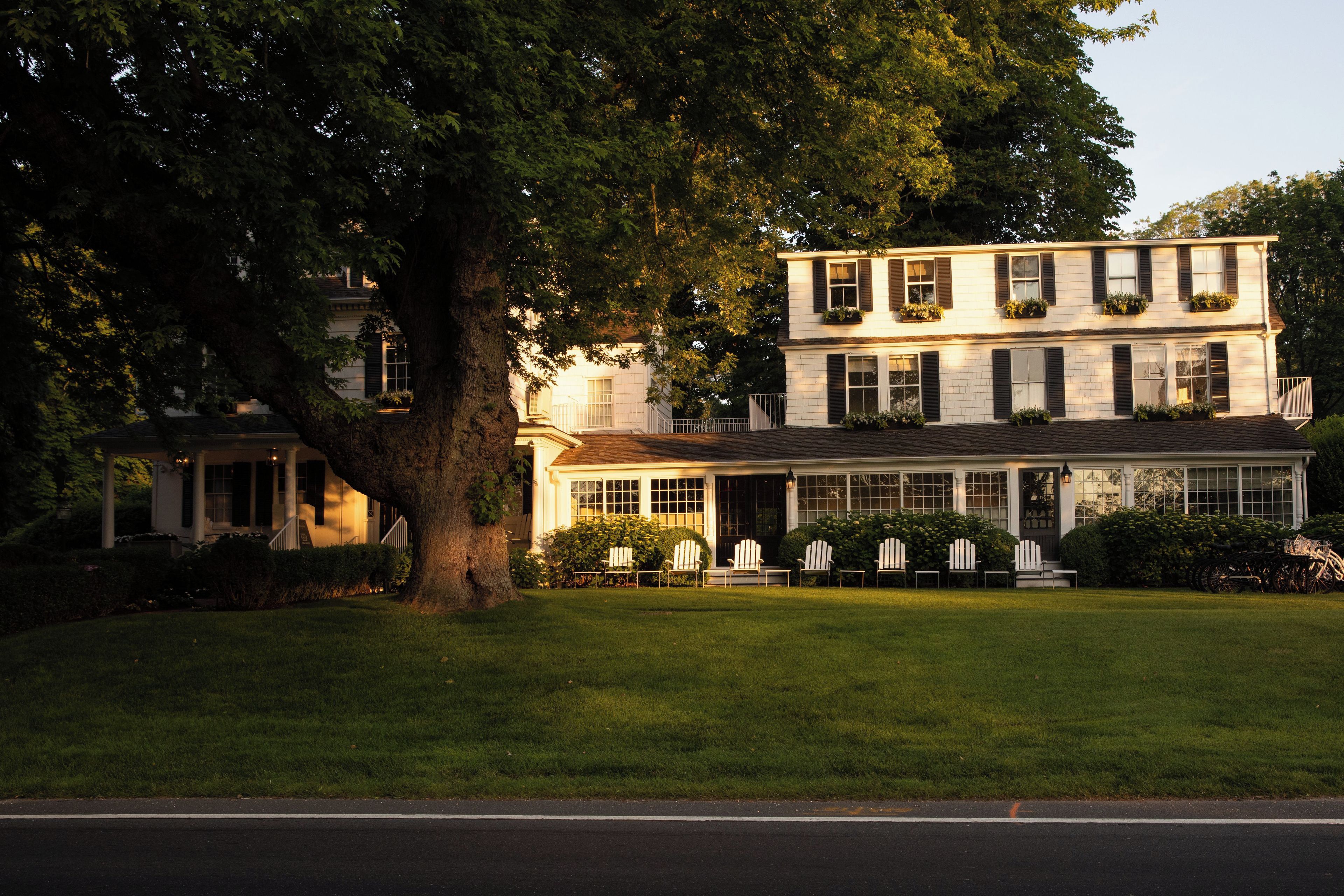 A two-story building with a porch and multiple windows, surrounded by greenery.