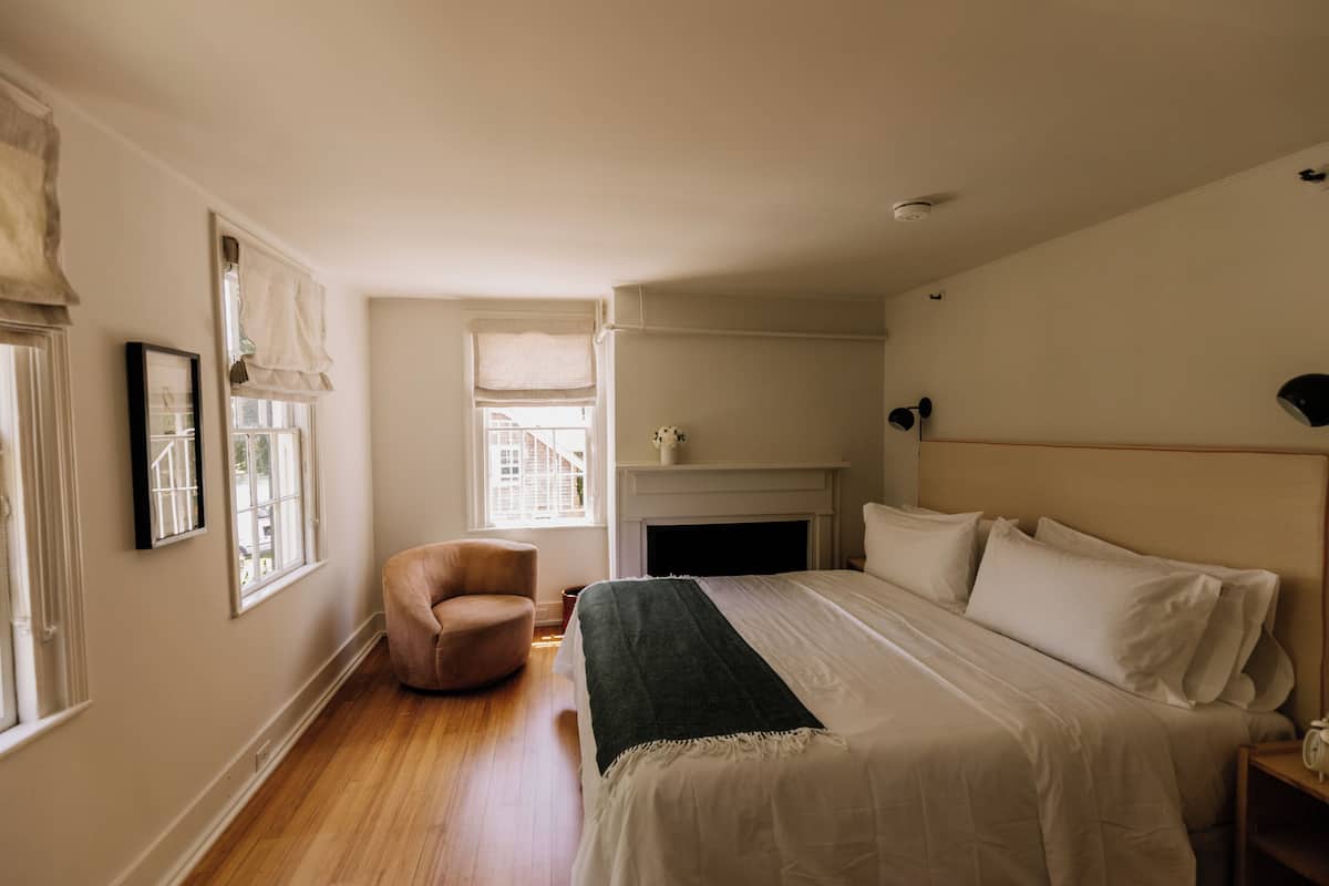 A bedroom with a large bed, a chair, a fireplace, and a window with curtains.