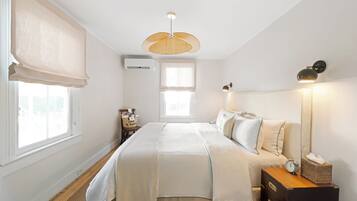 A bedroom with a bed, bedside table, lamp, and a window with blinds.