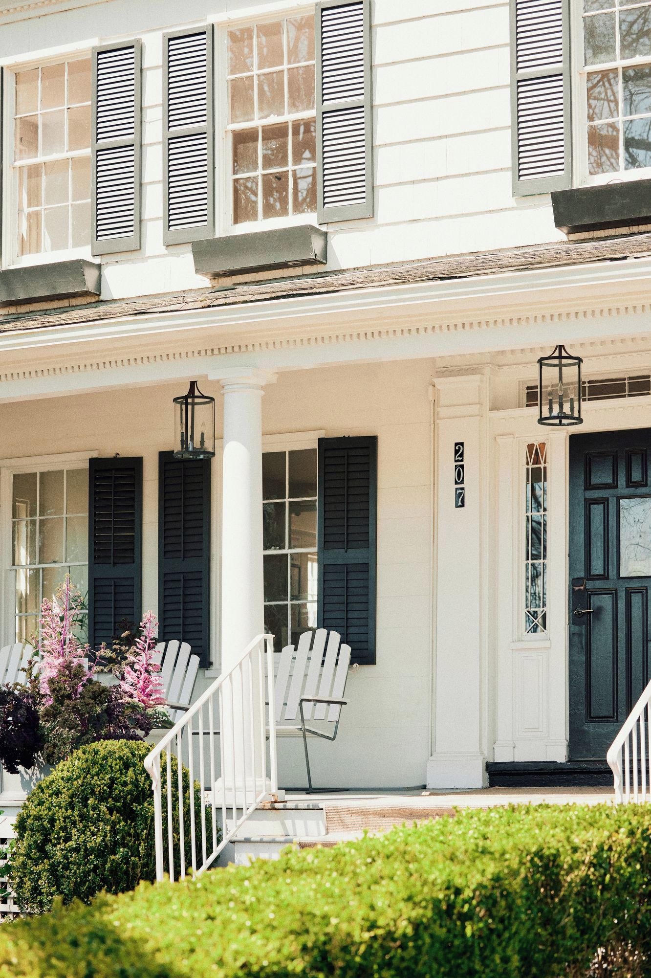 A two-story building with a porch, white railings, and a black door with a number.