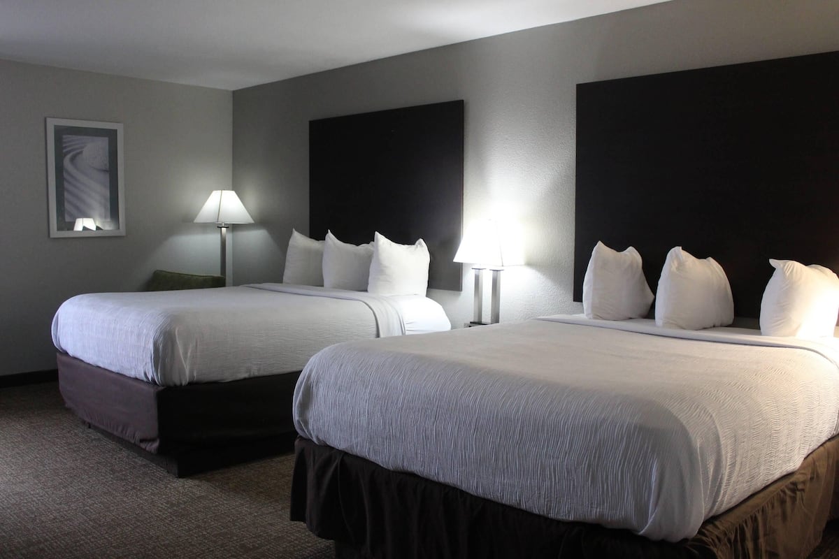 A hotel room with two beds, a large dark headboard, a framed picture on the wall, and a lamp on each side of the beds.