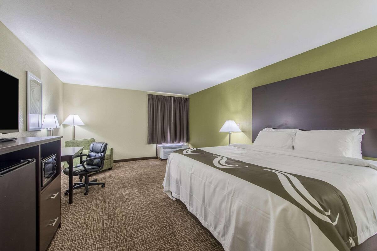 Ein Hotelzimmer mit Bett, Schreibtisch, Stuhl, Fernseher, Lampen und einer Klimaanlage.