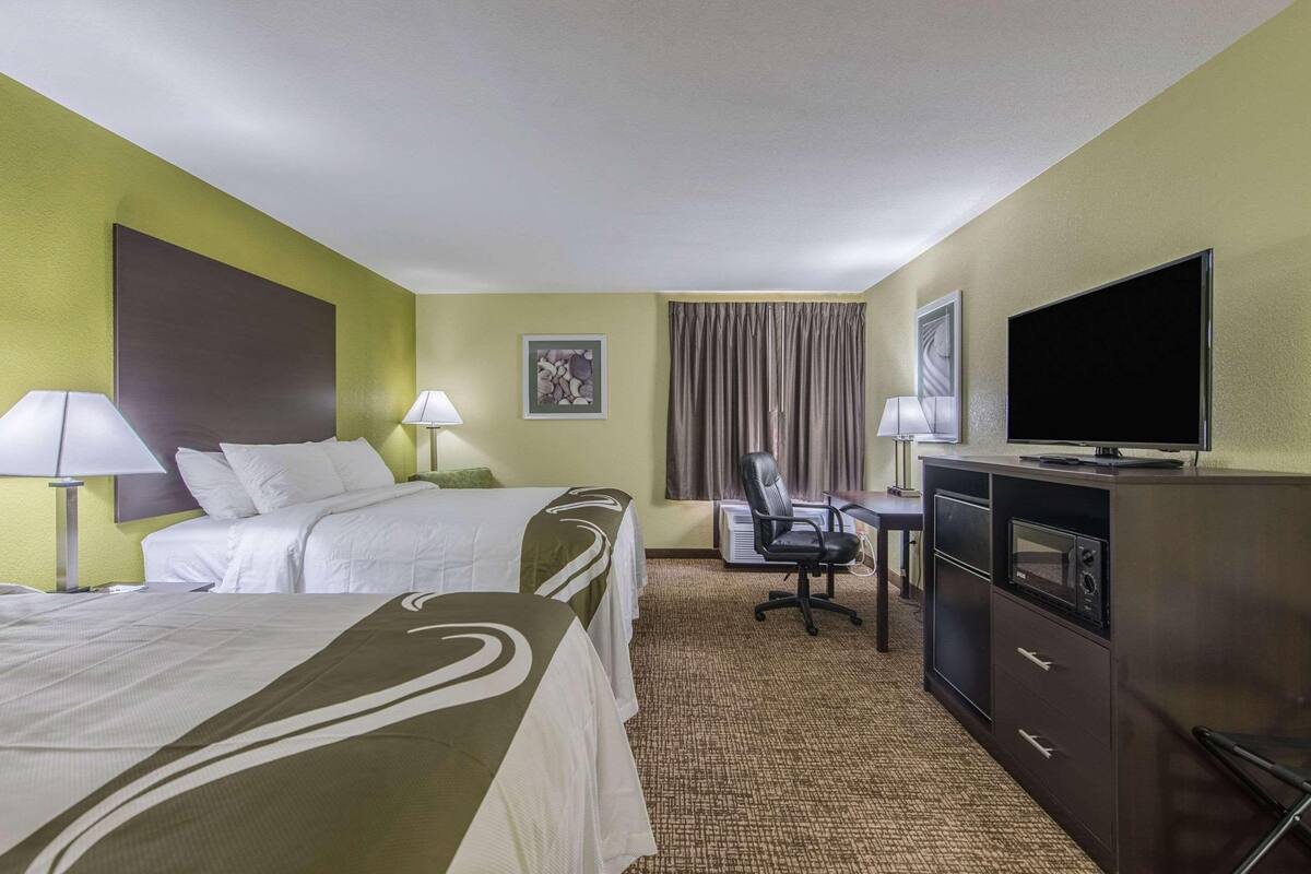 Ein Hotelzimmer mit zwei Betten, einem Schreibtisch mit Stuhl, einem Fernseher und einer Minibar.