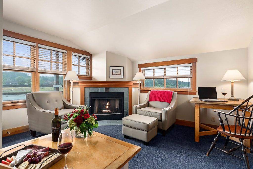 A cozy living room with a fireplace, comfortable seating, a dining table with a wine glass and flowers, and a laptop on a side table.