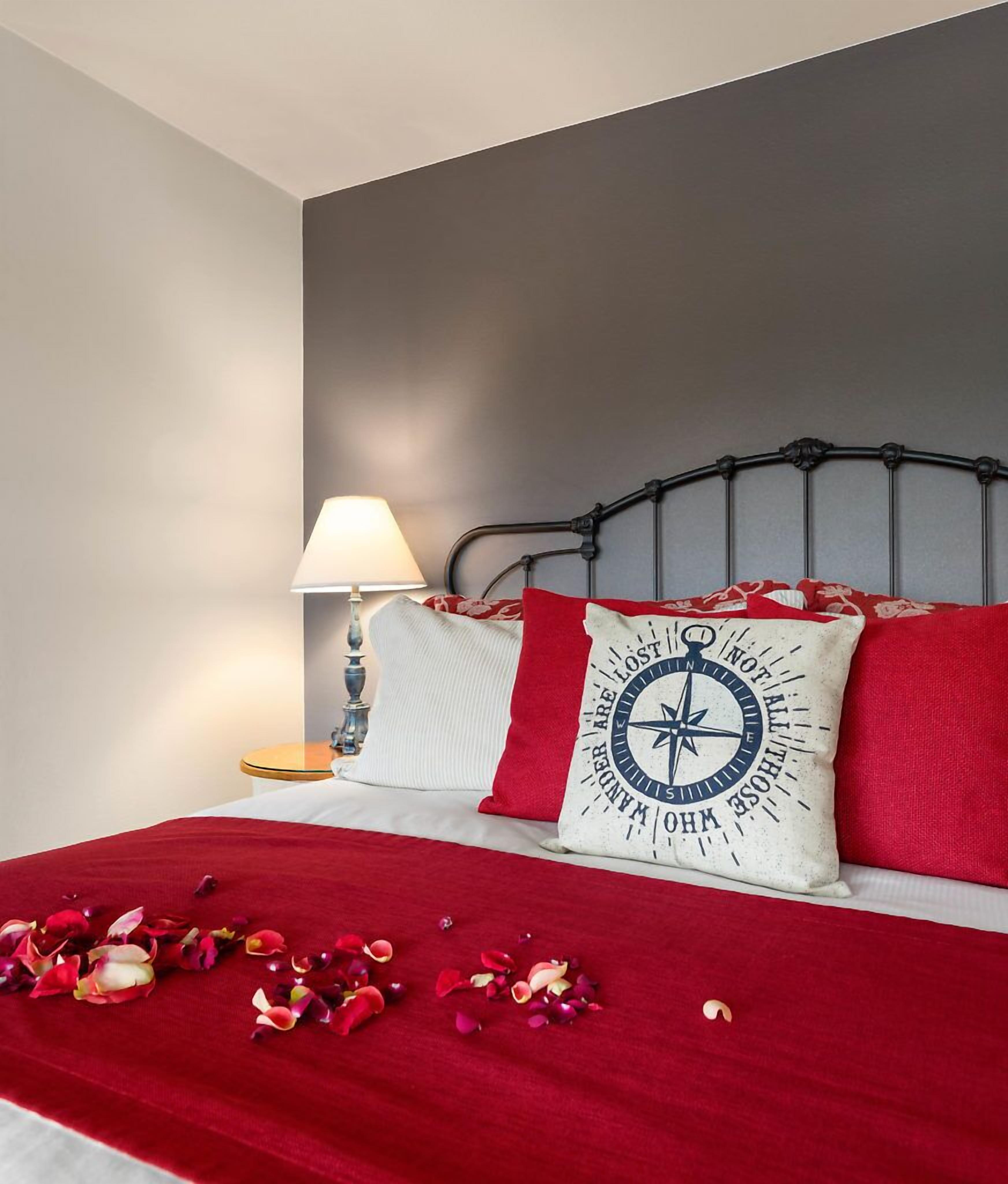 Un lit bien fait, recouvert d’une courtepointe rouge, avec un oreiller blanc orné d’un motif de boussole et un oreiller rouge avec un motif textuel.