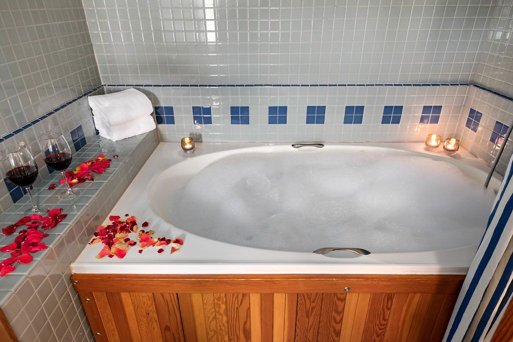 A bathroom with a bathtub, a towel rack, and rose petals on the floor.
