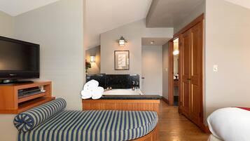 A modern hotel room with a curved seating area, a flat-screen TV, a small kitchen with a sink, and a wooden wardrobe.