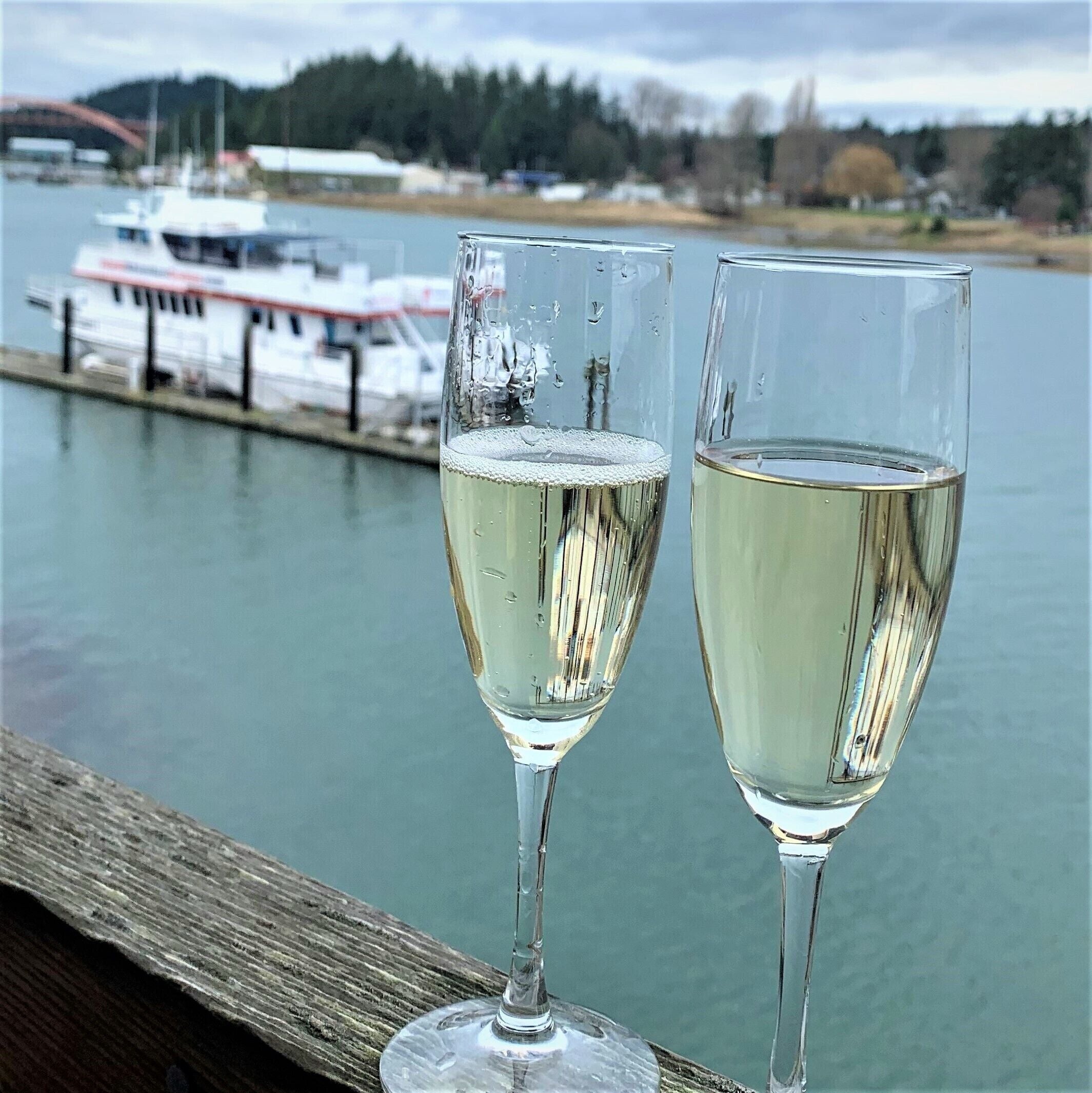 Two glasses of white wine on a wooden surface with a body of water and a boat in the background.