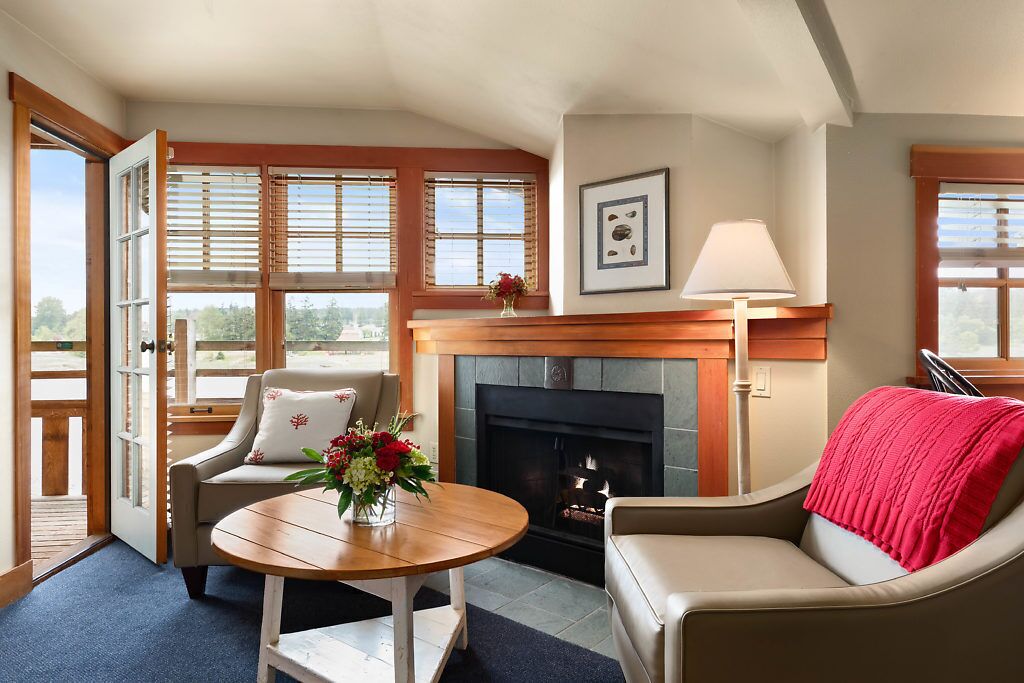 A cozy living room with a fireplace, a sofa, a chair, and a table with a vase of flowers.
