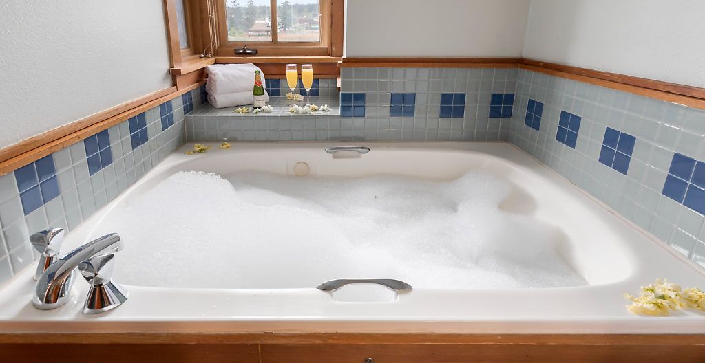 A large bathtub with a wooden frame, a window above it, and a tiled backsplash.