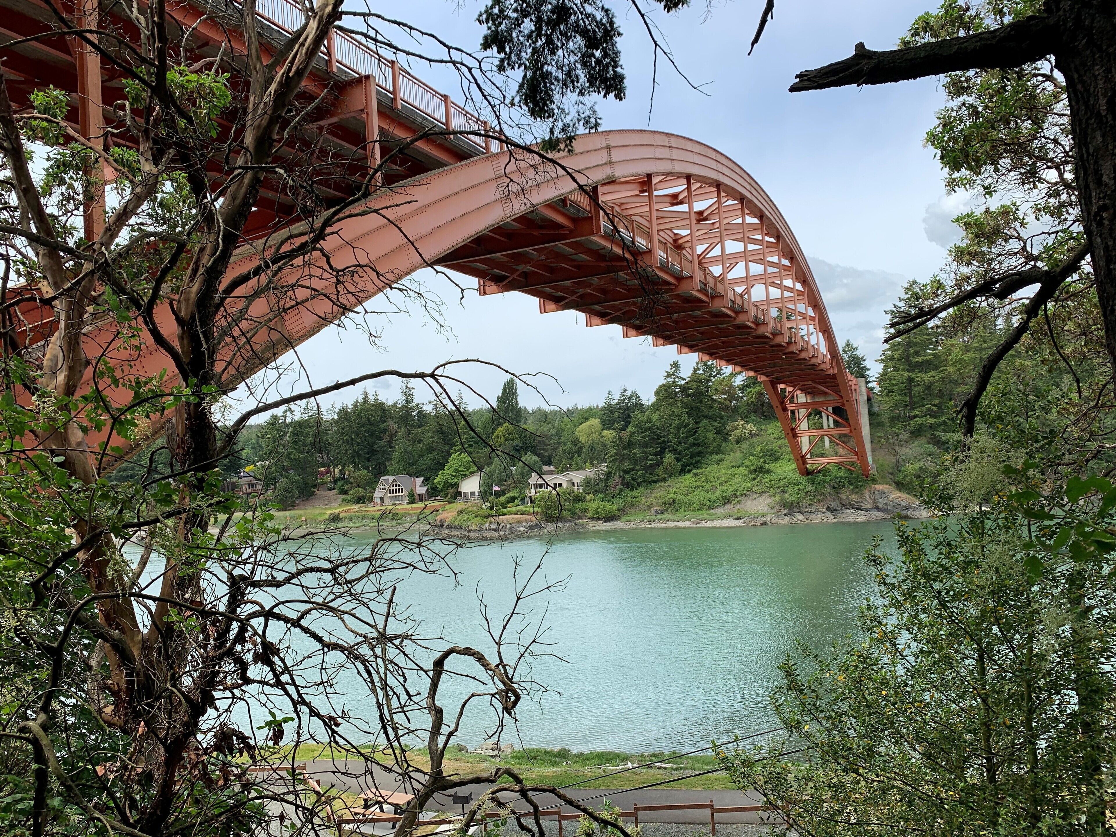 A red steel bridge over a calm lake with houses in the background.