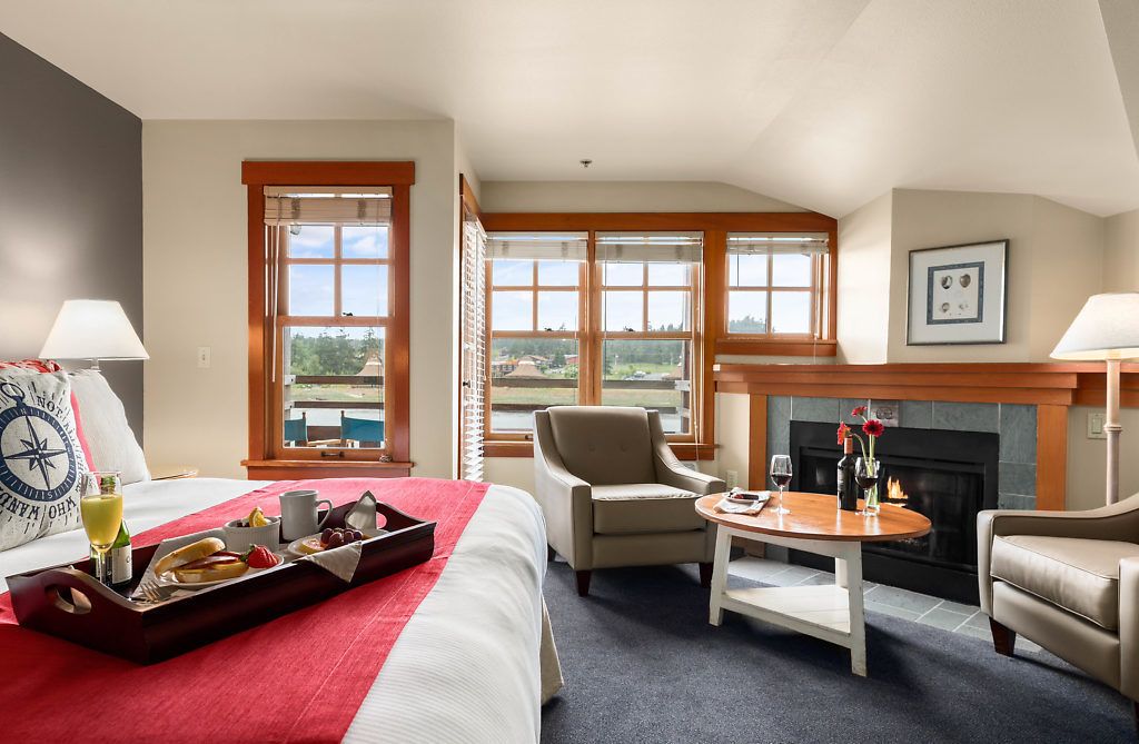 A hotel room with a bed, a fireplace, a dining table, and a view of the outdoors.