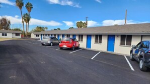 A motel with a row of rooms, each with a blue door, and a parking lot with several cars. - Chandler Inn (Chandler)