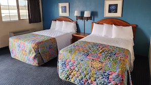 Ein Hotelzimmer mit zwei Betten, jedes mit einer farbenfrohen Steudecke, einem Fenster mit Vorhängen, einer wandmontierten Klimaanlage und zwei Wandlampen.