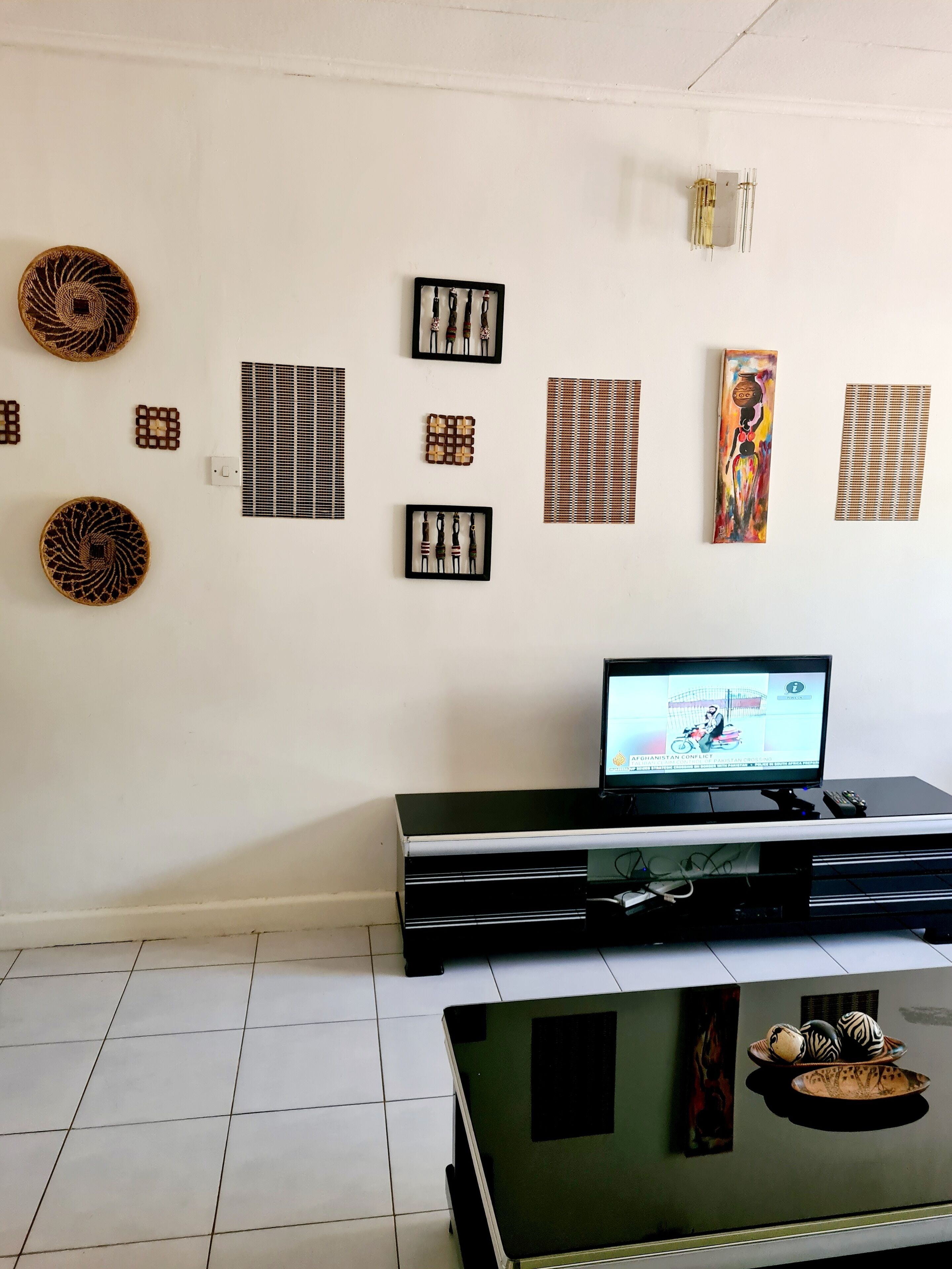 A living room with a flat-screen TV, a black entertainment unit, and various framed artworks on the wall.
