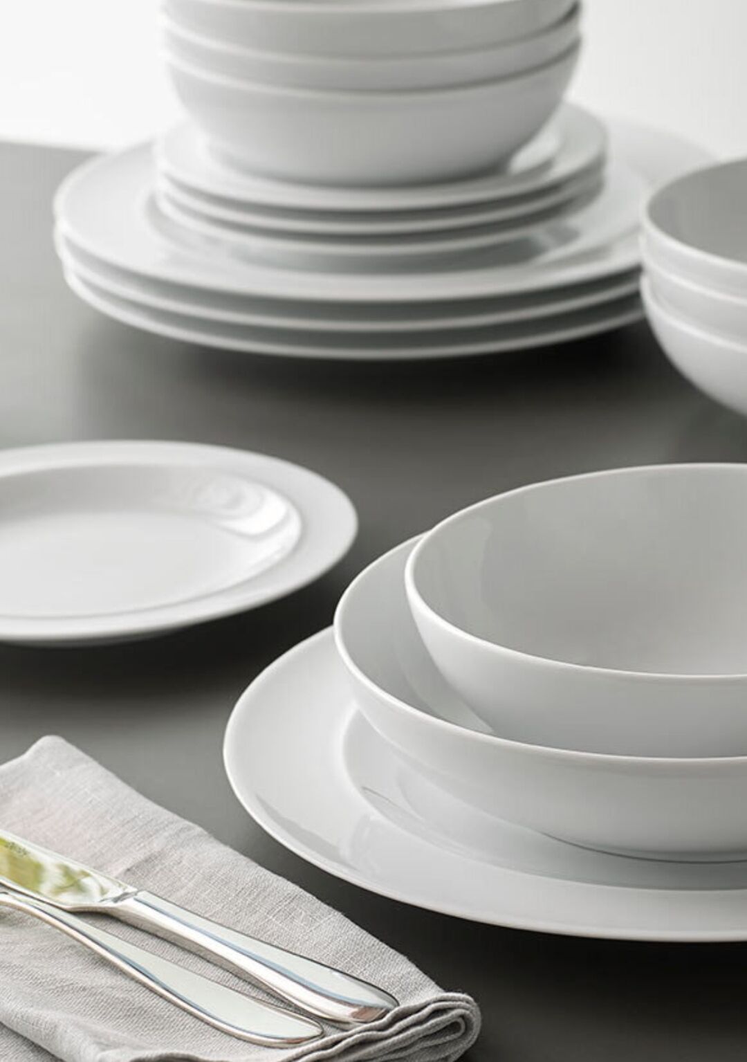 A stack of white plates and bowls on a dark surface.