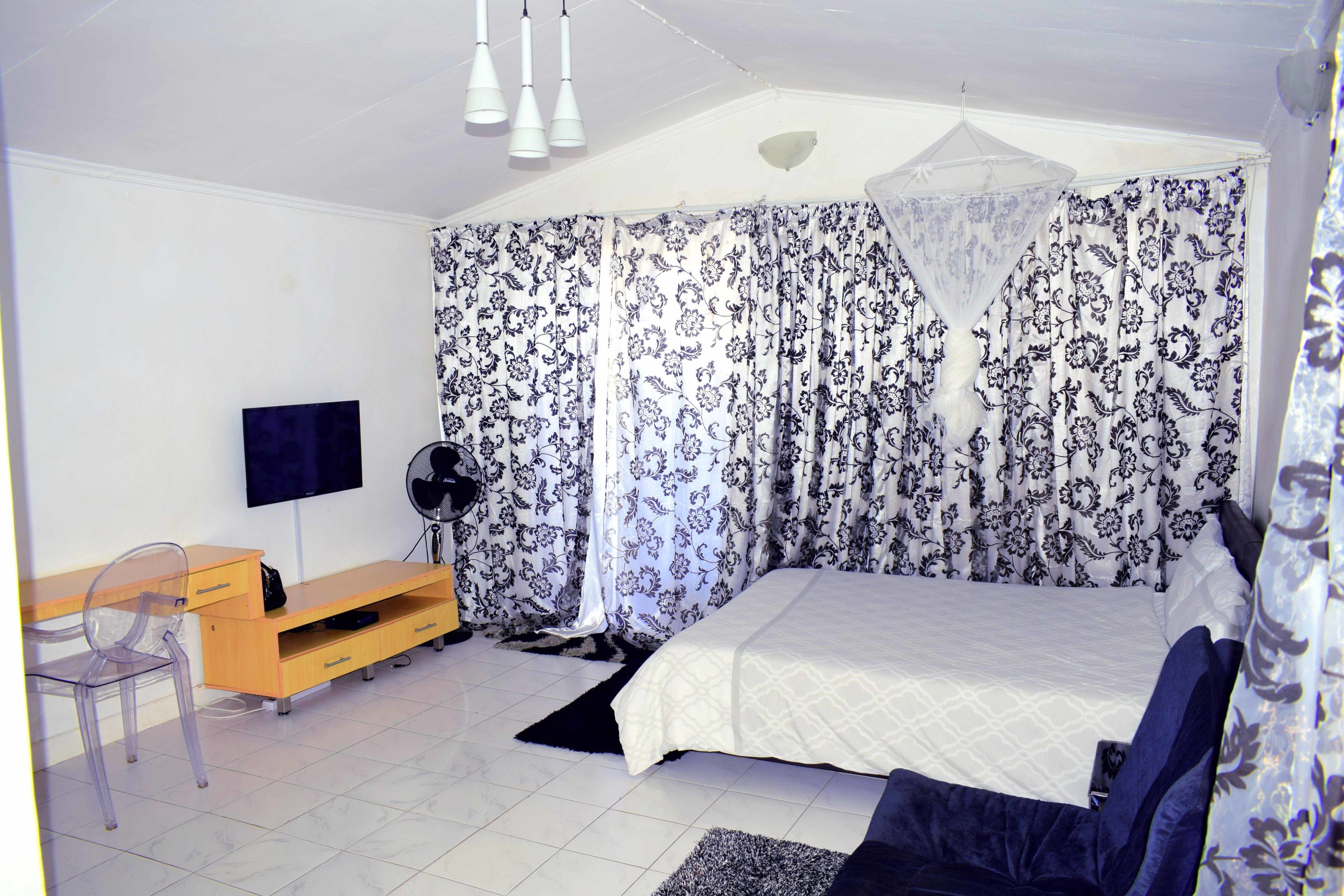 A bedroom with a bed, a desk, a chair, a TV, and curtains.