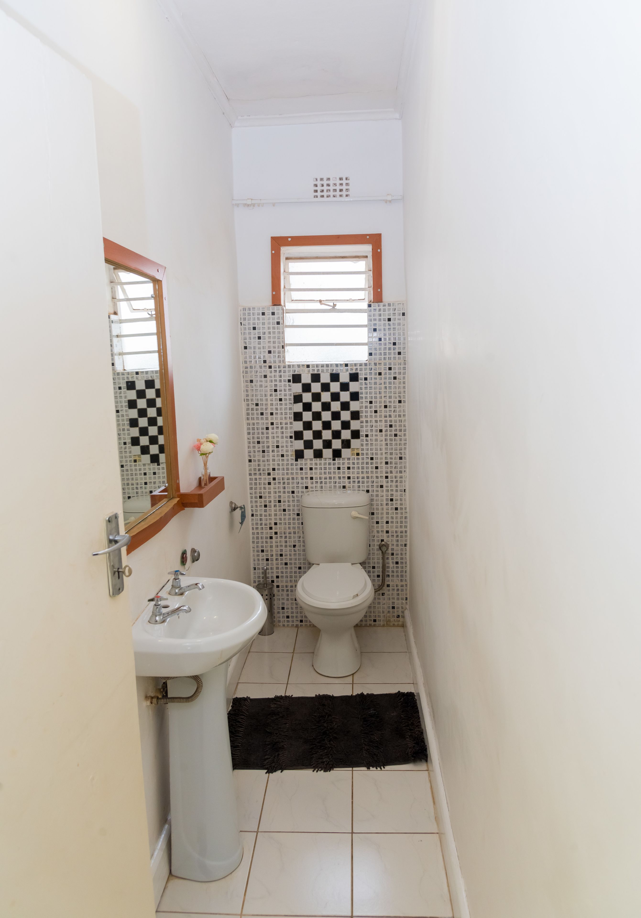 A narrow bathroom with a white sink, a toilet, and a mirror.