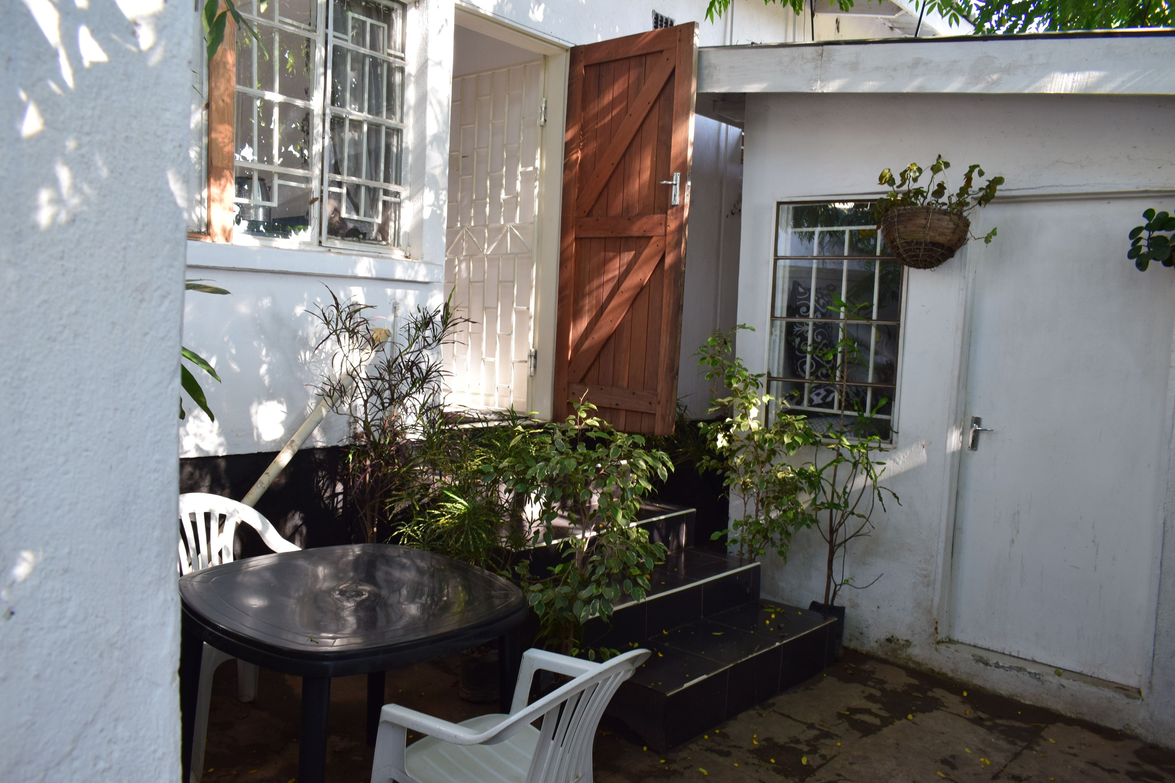 Un pequeño patio con una mesa, sillas, una puerta de madera y plantas en macetas.