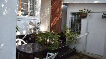Un pequeño patio con una mesa, sillas, una puerta de madera y plantas en macetas.