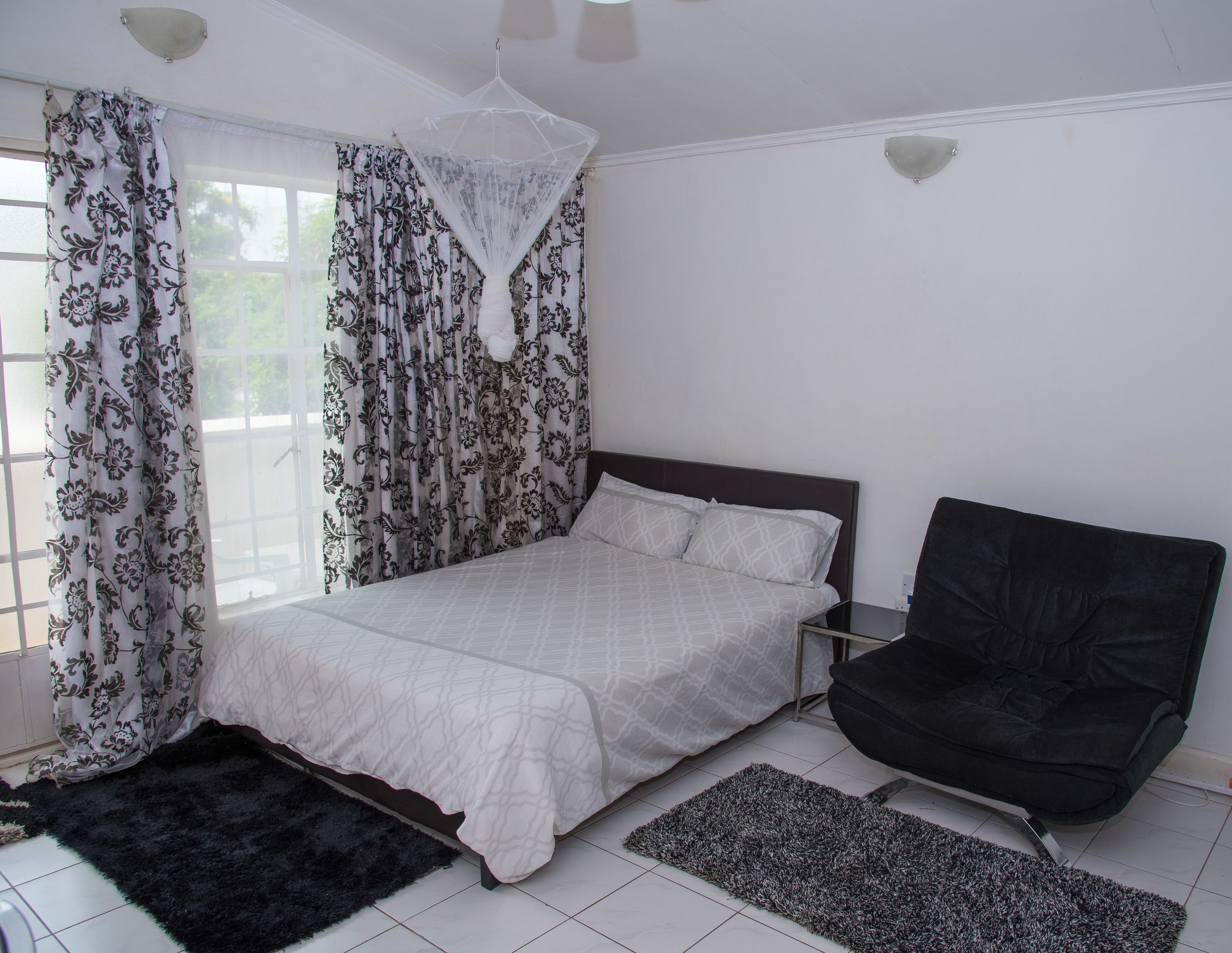 Un dormitorio con una cama, una silla negra y una ventana con cortinas estampadas.