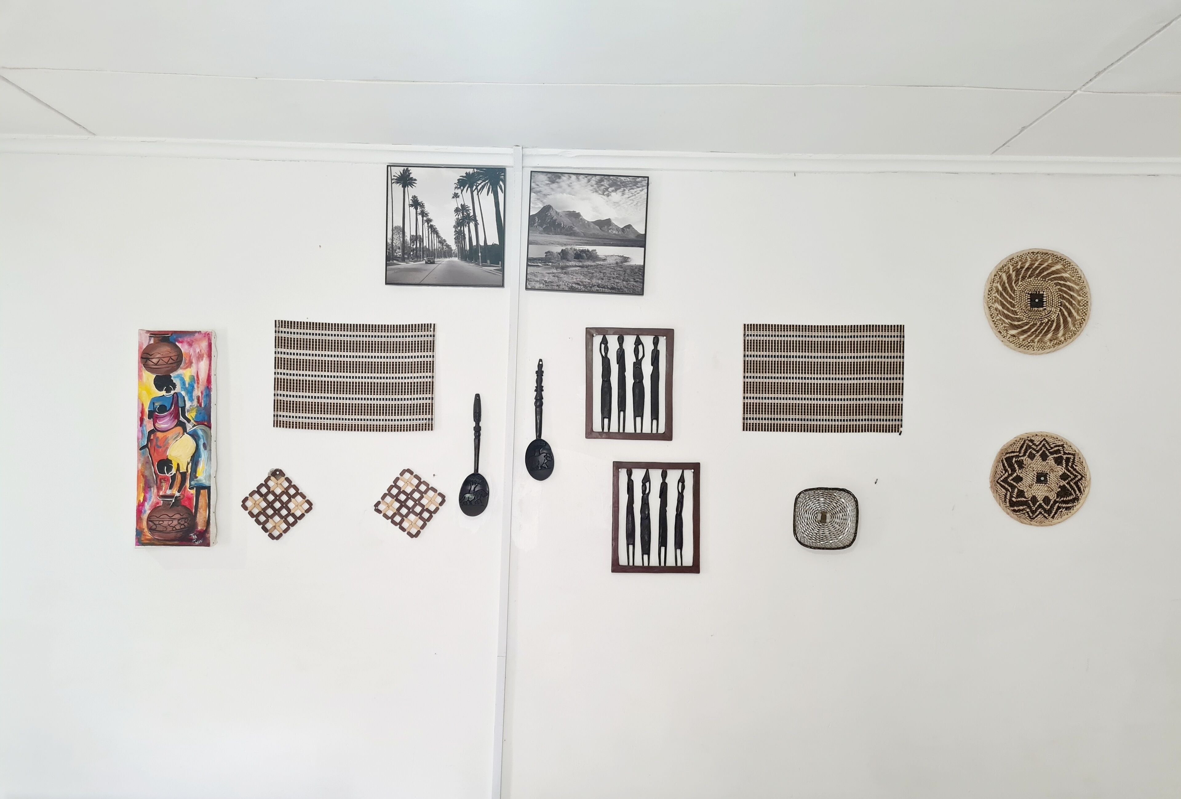 Un mur orné de diverses œuvres d’art et d’objets décoratifs, notamment des photographies encadrées, une peinture colorée et des objets tissés.