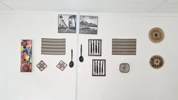 Un mur orné de diverses œuvres d’art et d’objets décoratifs, notamment des photographies encadrées, une peinture colorée et des objets tissés.