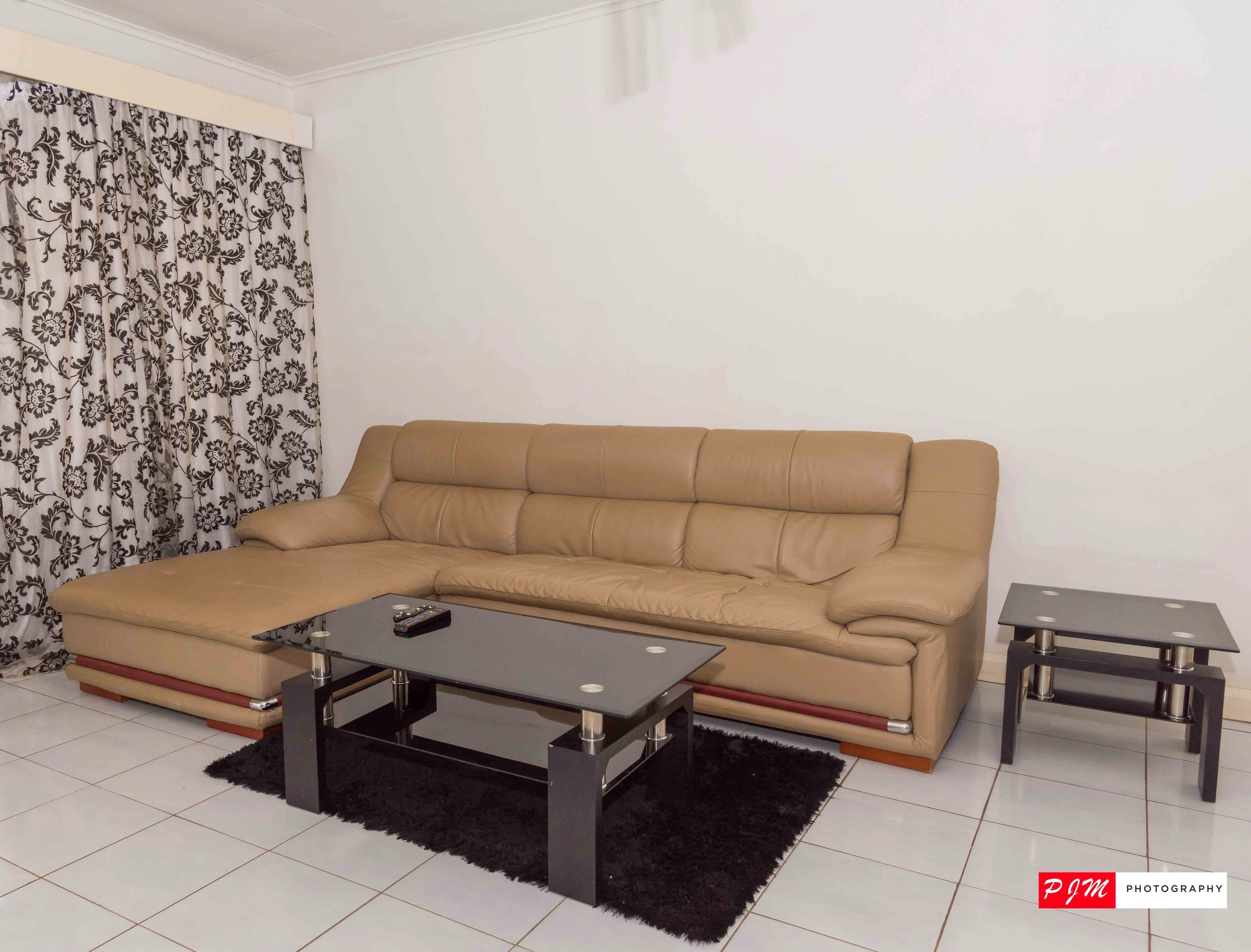 Un salon avec un canapé d’angle beige, une table basse en verre et une table d’appoint assortie.