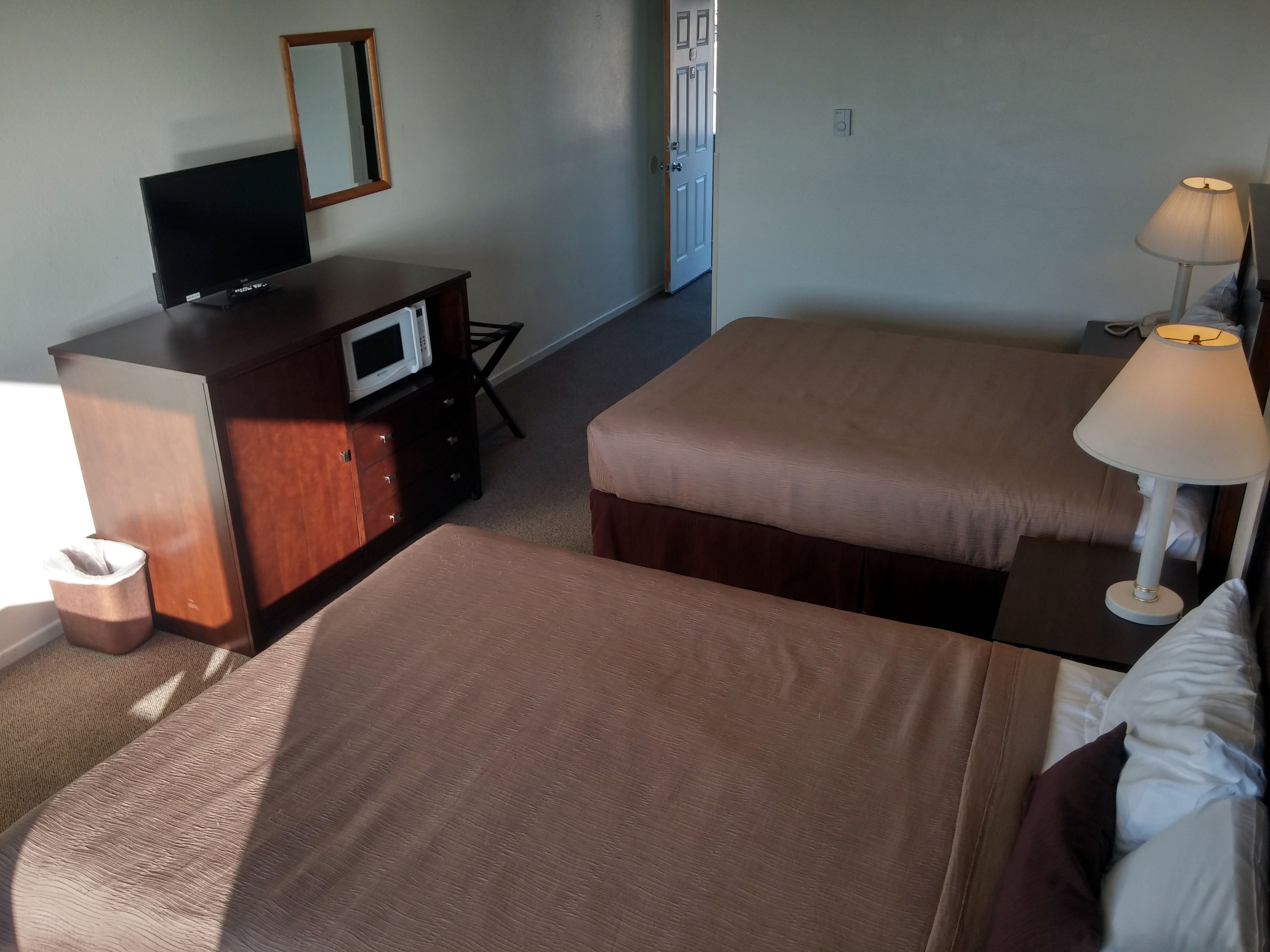 Una habitación de hotel con cama, escritorio con televisor, lámpara y puerta.