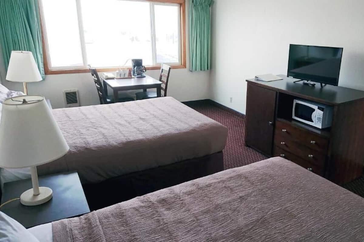 Quarto de hotel com duas camas, uma escrivaninha, uma televisão e um micro-ondas.