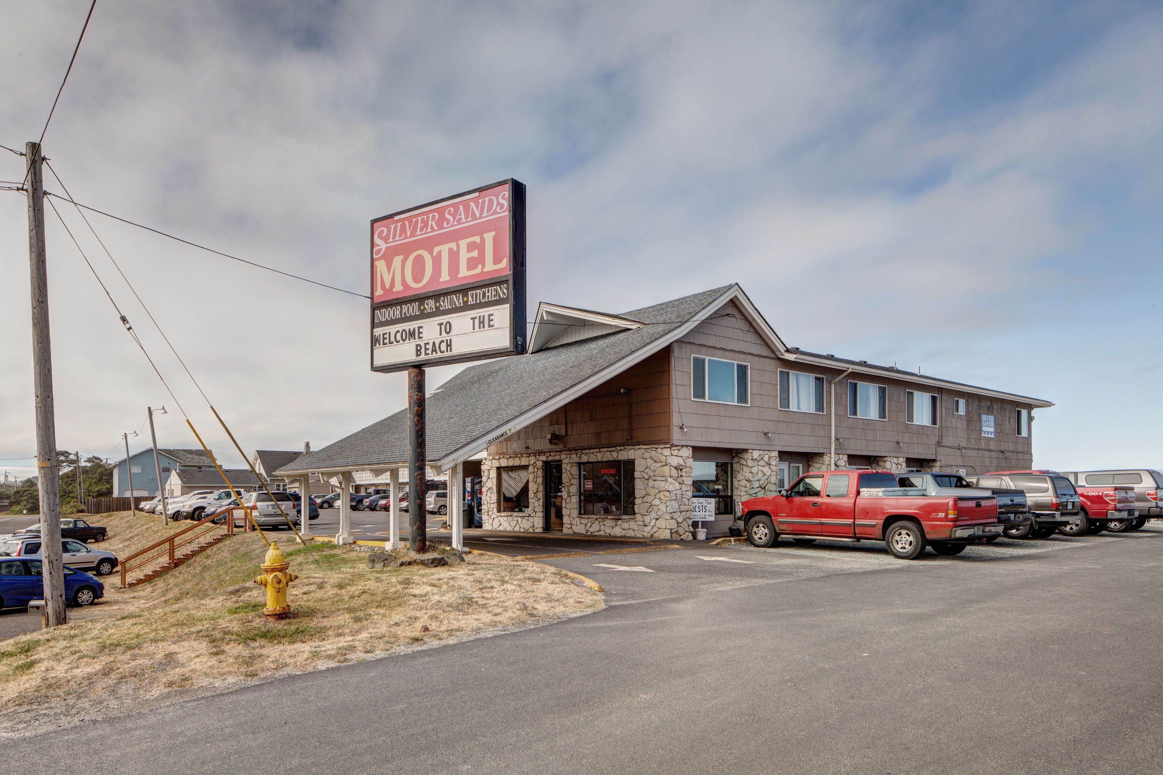 A motel with a stone facade, a signboard, and a parking lot with several vehicles.
