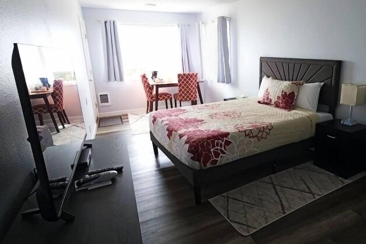 Quarto de hotel com cama, escrivaninha, cadeira, televisão e frigorífico.