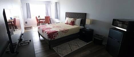 Une chambre d’hôtel équipée d’un lit, d’un bureau, d’une chaise, d’une télévision et d’un réfrigérateur.
