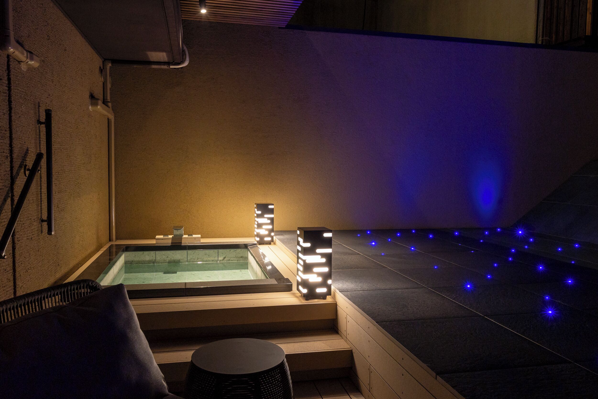 A spa area with a hot tub, steps, and illuminated pillars.