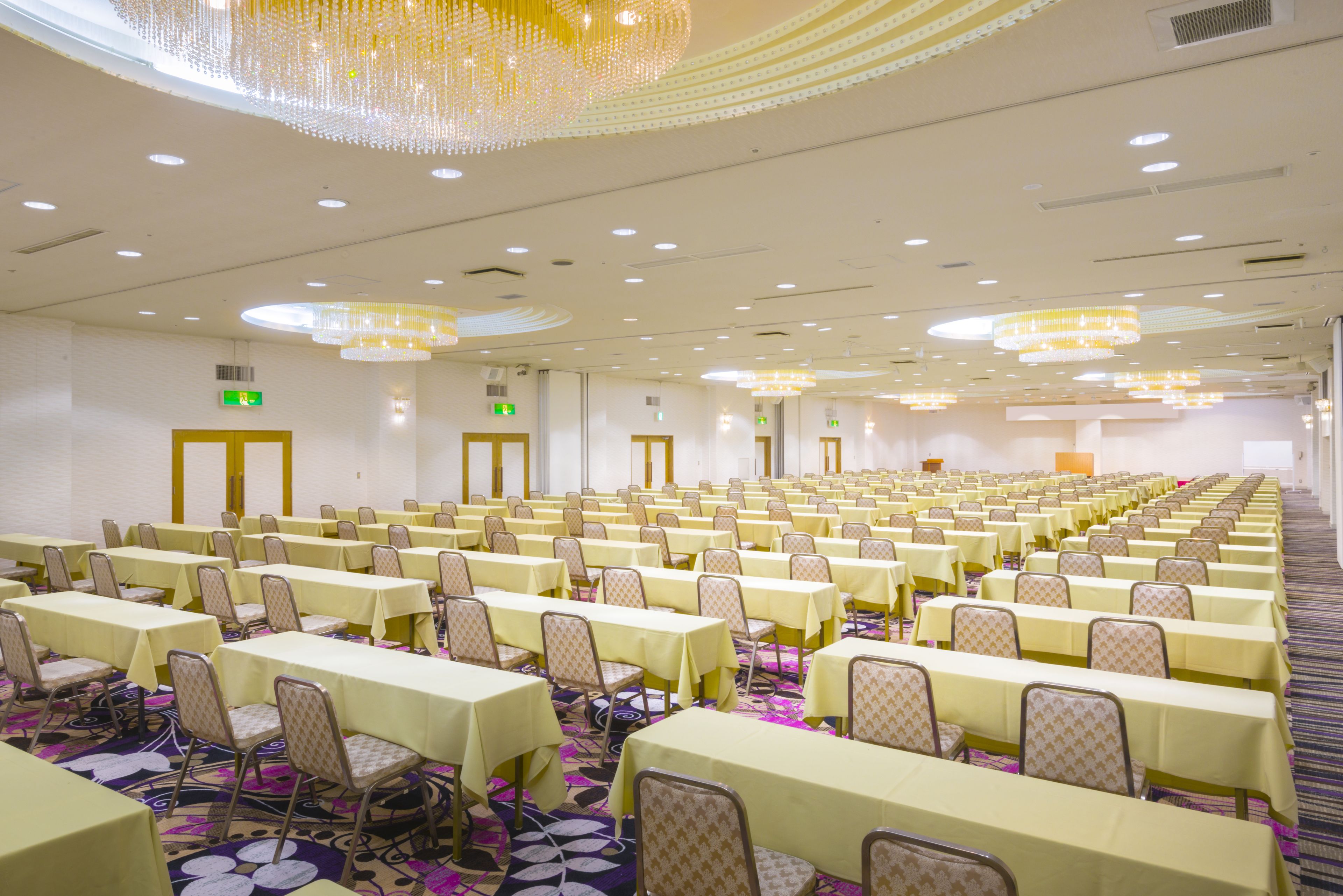Un amplio salón de conferencias con filas de mesas y sillas, equipado con candelabros e iluminación del techo.