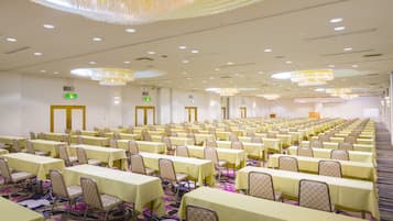 Un amplio salón de conferencias con filas de mesas y sillas, equipado con candelabros e iluminación del techo.