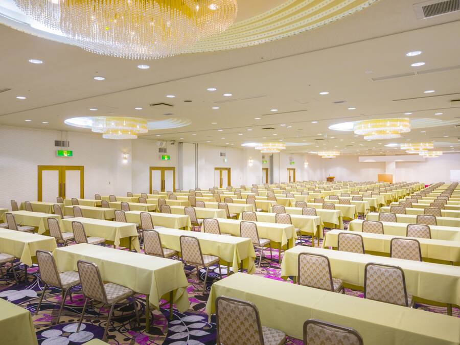 Un amplio salón de conferencias con filas de mesas y sillas, equipado con candelabros e iluminación del techo.