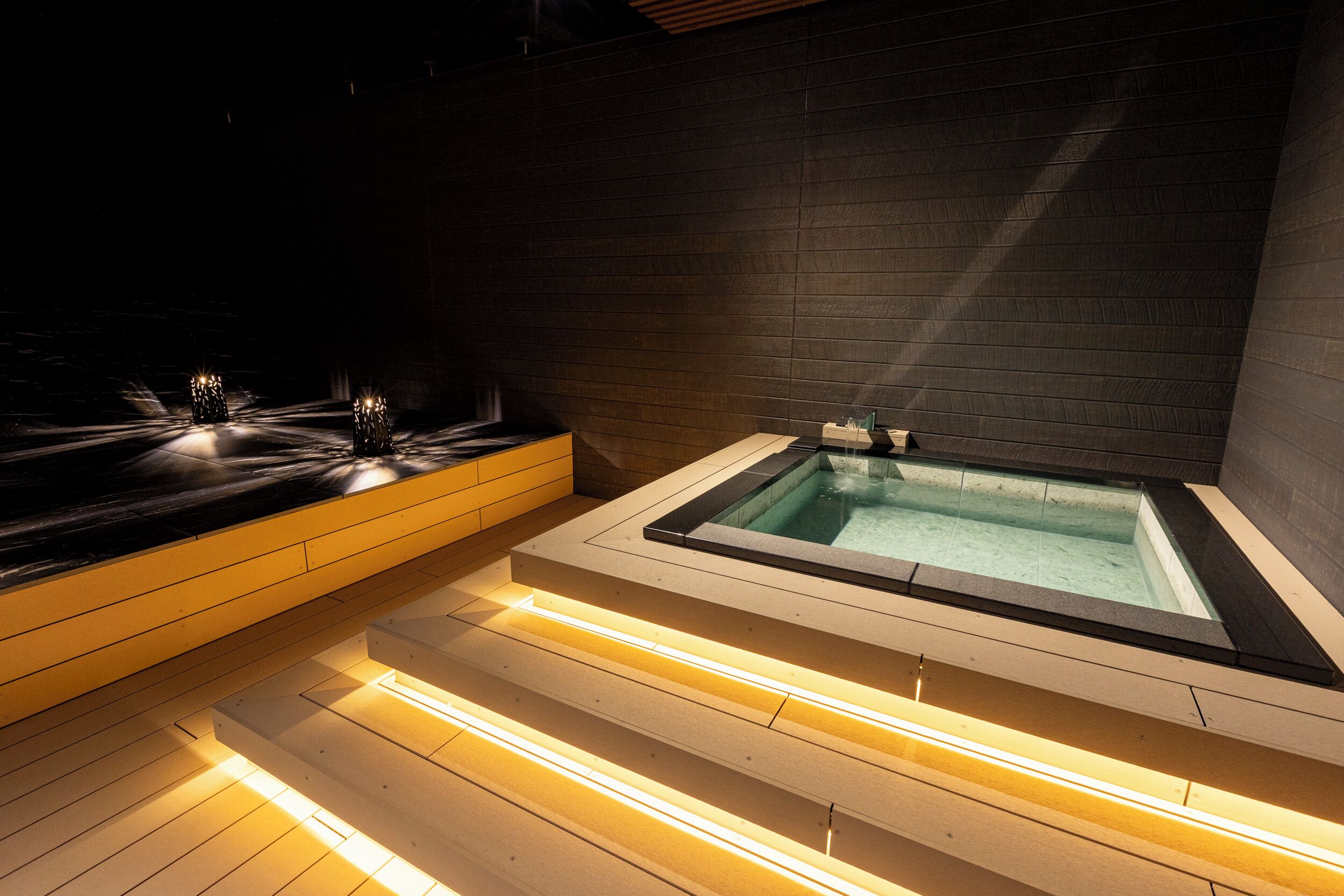 A modern spa area with a hot tub, wooden steps, and ambient lighting.