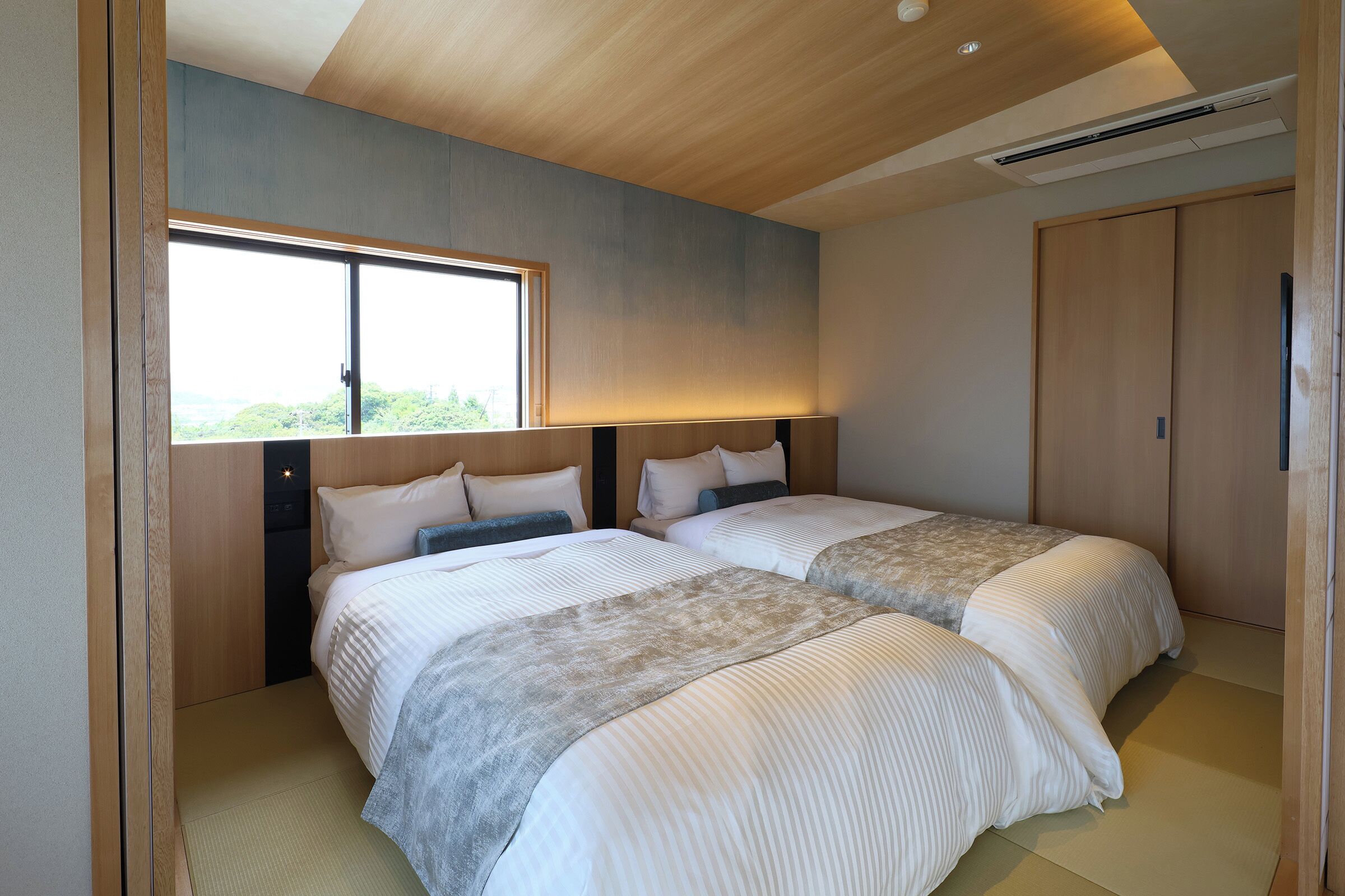 Une chambre d’hôtel moderne avec deux lits, une grande fenêtre et un plafond en bois.