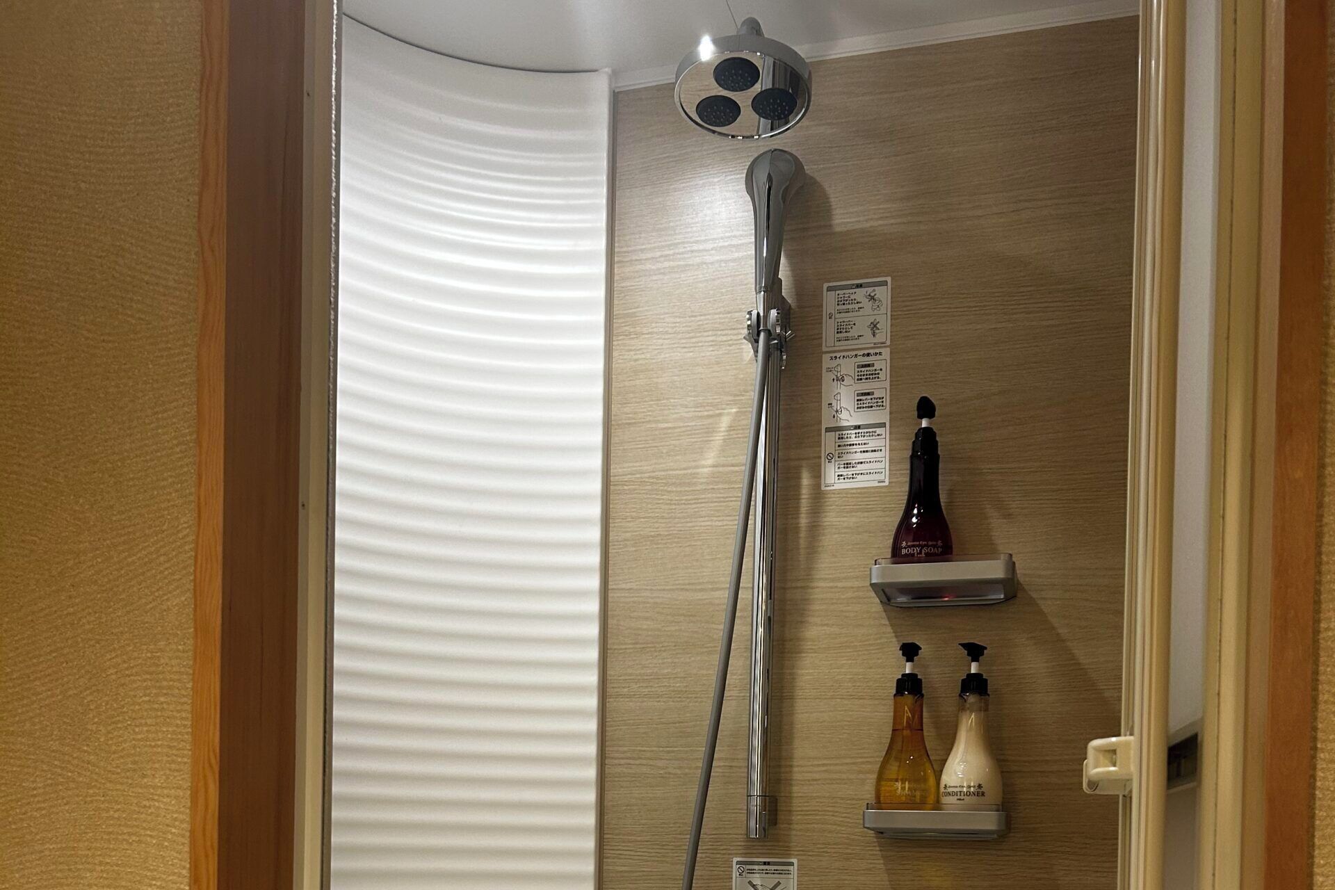 A shower with a handheld showerhead, a wall-mounted control panel, and a shelf with body soap and conditioner bottles.