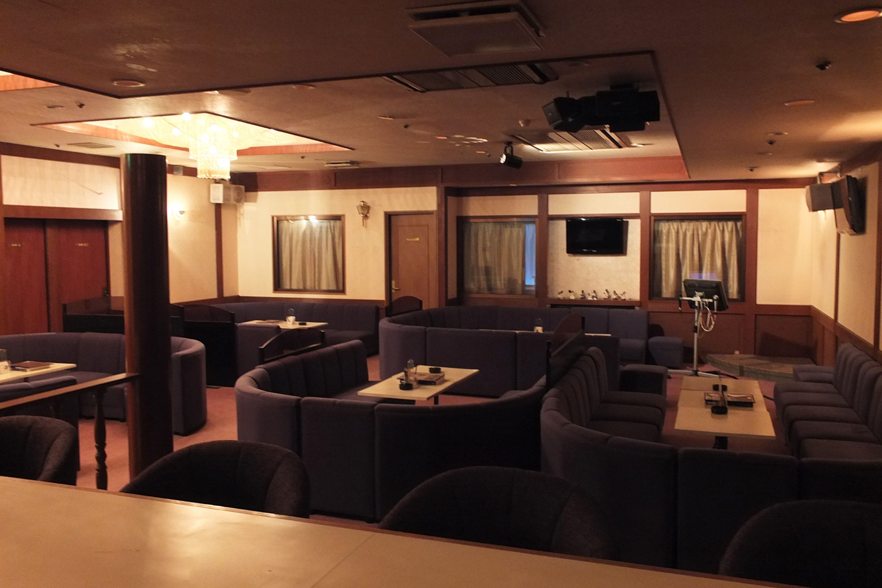 A restaurant with booth seating and tables, a chandelier, and a television screen on the wall.