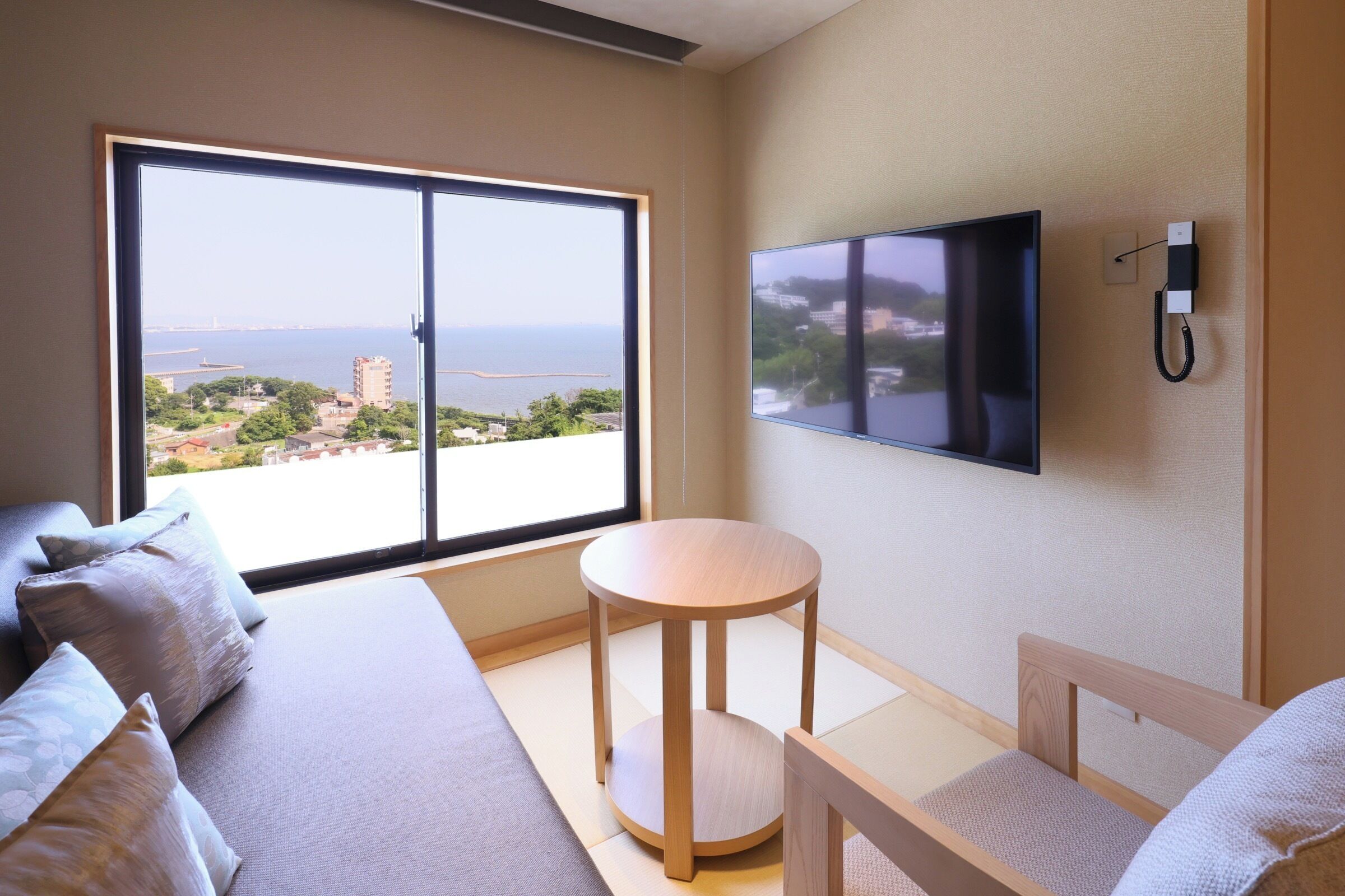Habitación de hotel moderna con un ventanal grande que ofrece vistas a la ciudad, un televisor de pantalla plana en la pared y una pequeña mesa redonda.