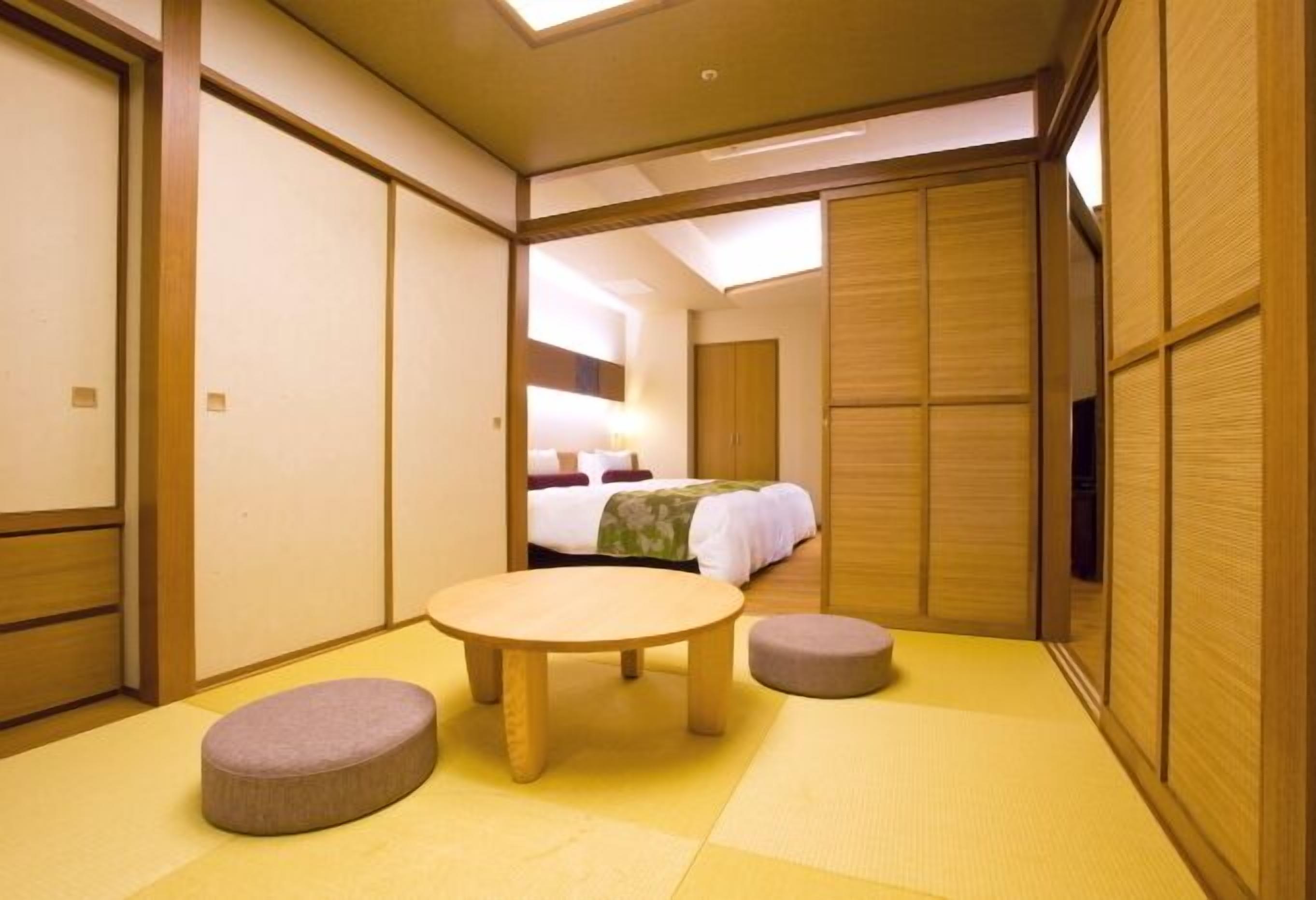 A traditional Japanese-style room with tatami flooring, a round wooden table, two tatami cushions, and sliding wooden doors.