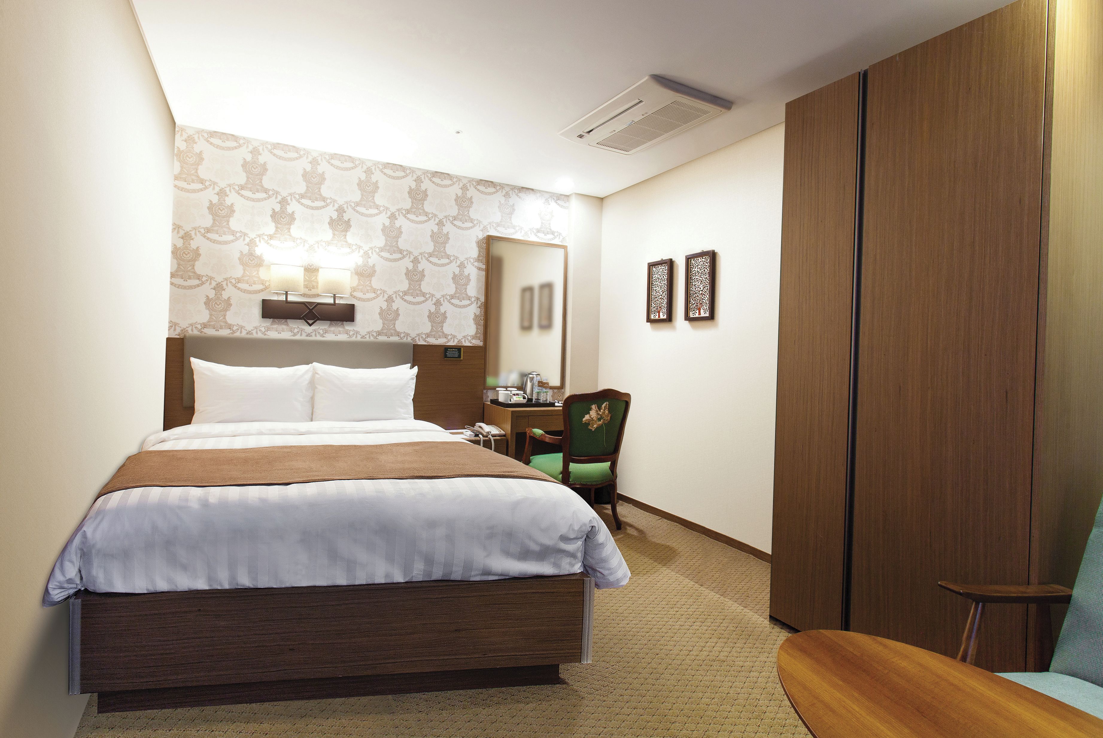 Une chambre d’hôtel avec un grand lit, un bureau avec une chaise, une armoire et un miroir au mur.