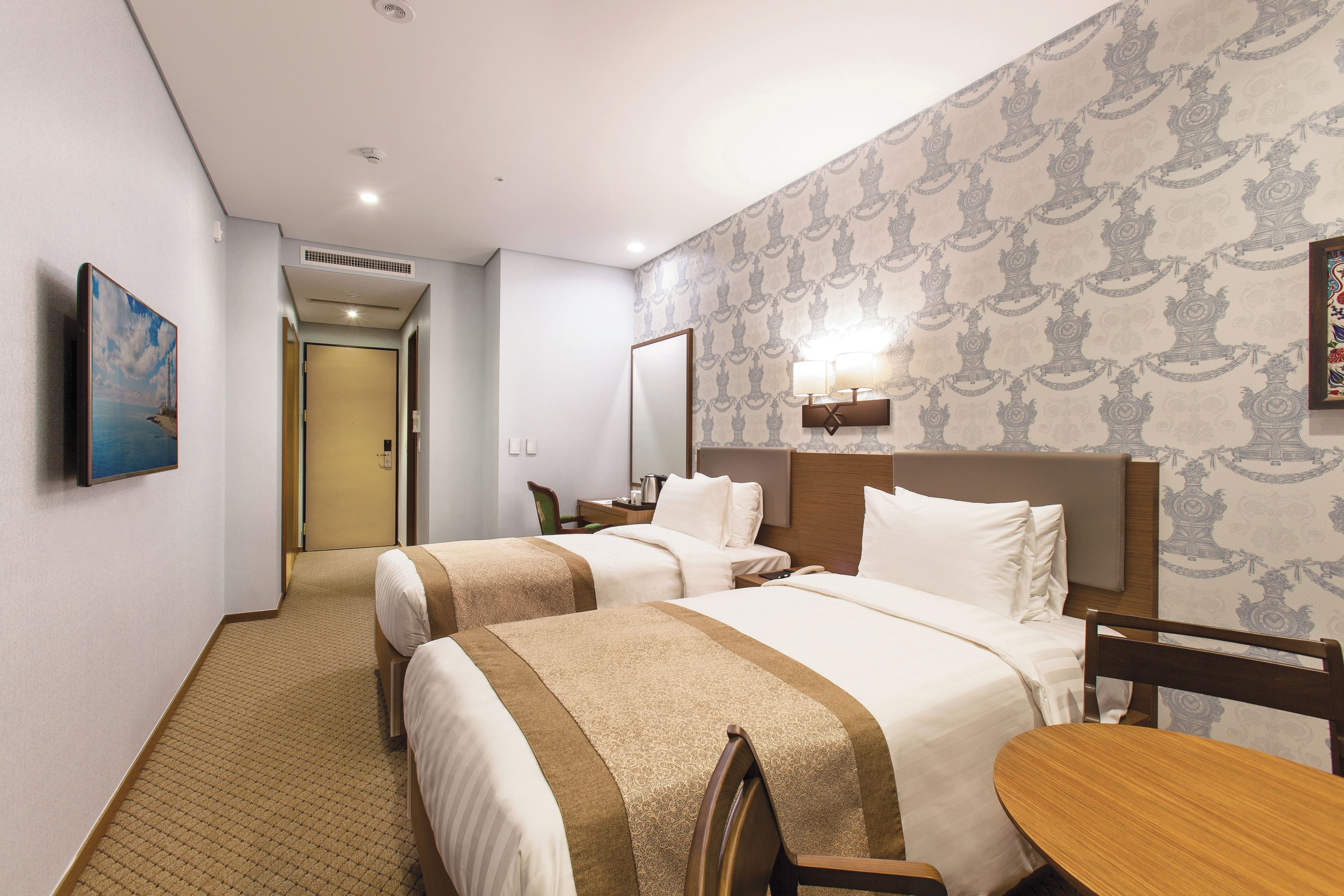 Une chambre d’hôtel avec deux lits, une table en bois, une chaise, un téléviseur et un tableau au mur.