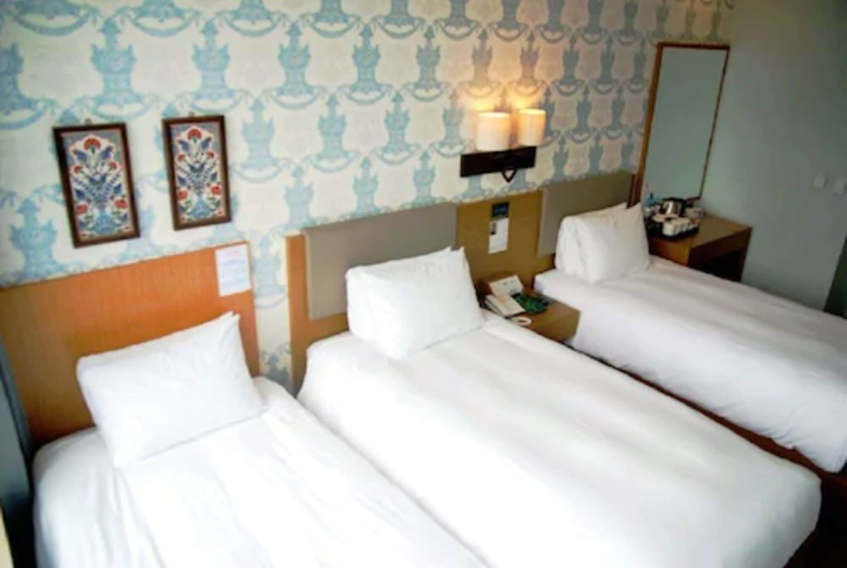 A hotel room with two single beds, a nightstand with a phone, and a wall-mounted lamp.